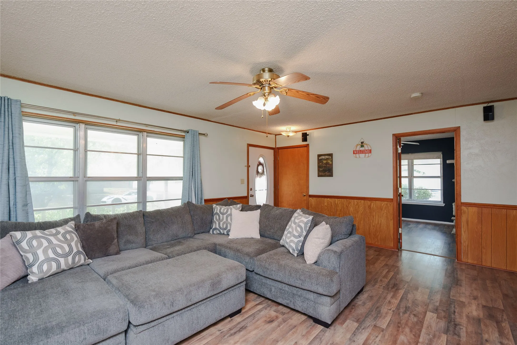 Living area with wood-finish flooring, wood paneling, multiple windows, and a ceiling fan