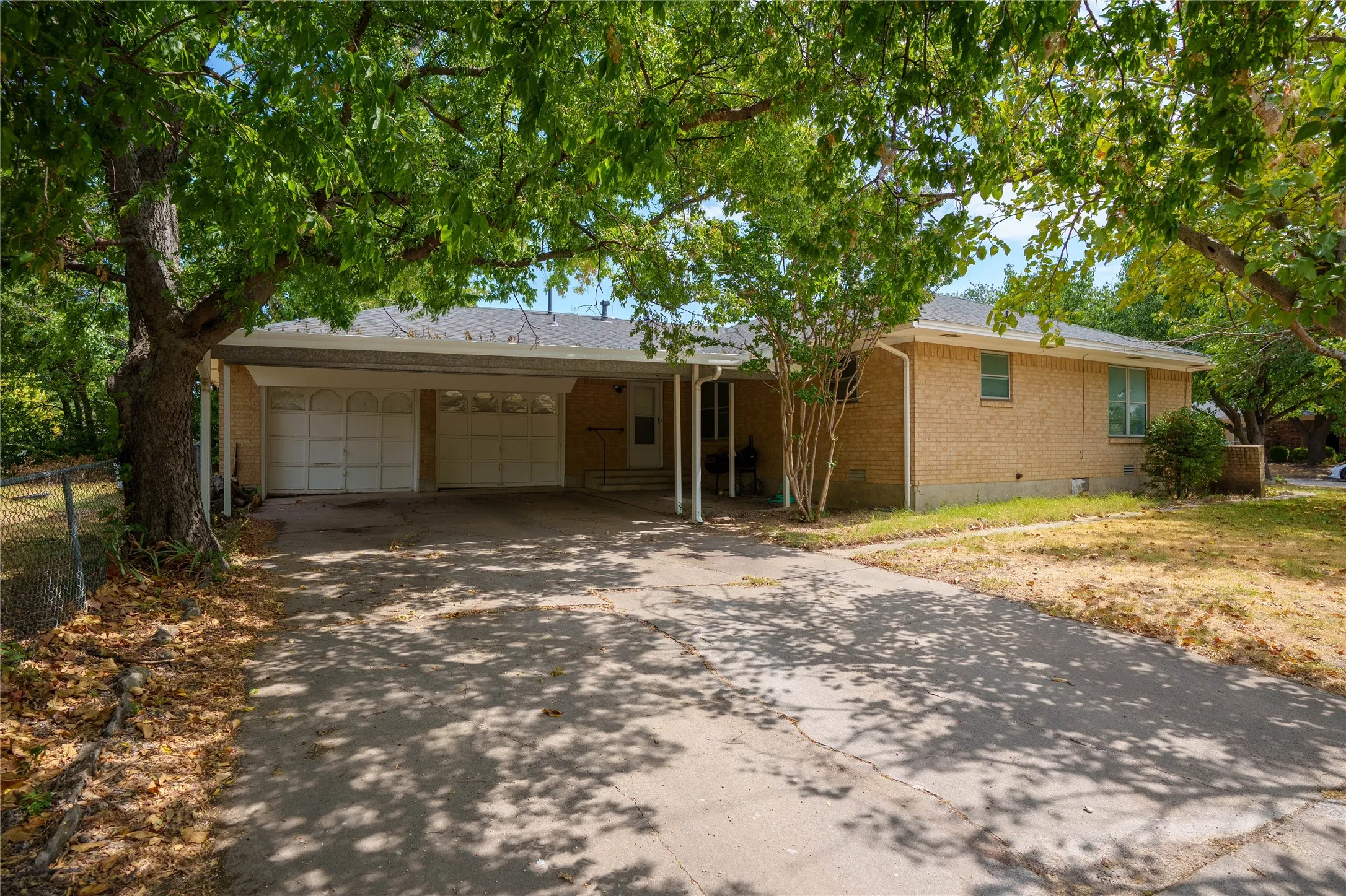 Brick exterior residence featuring a covered carport, two garage doors, and mature trees providing shade