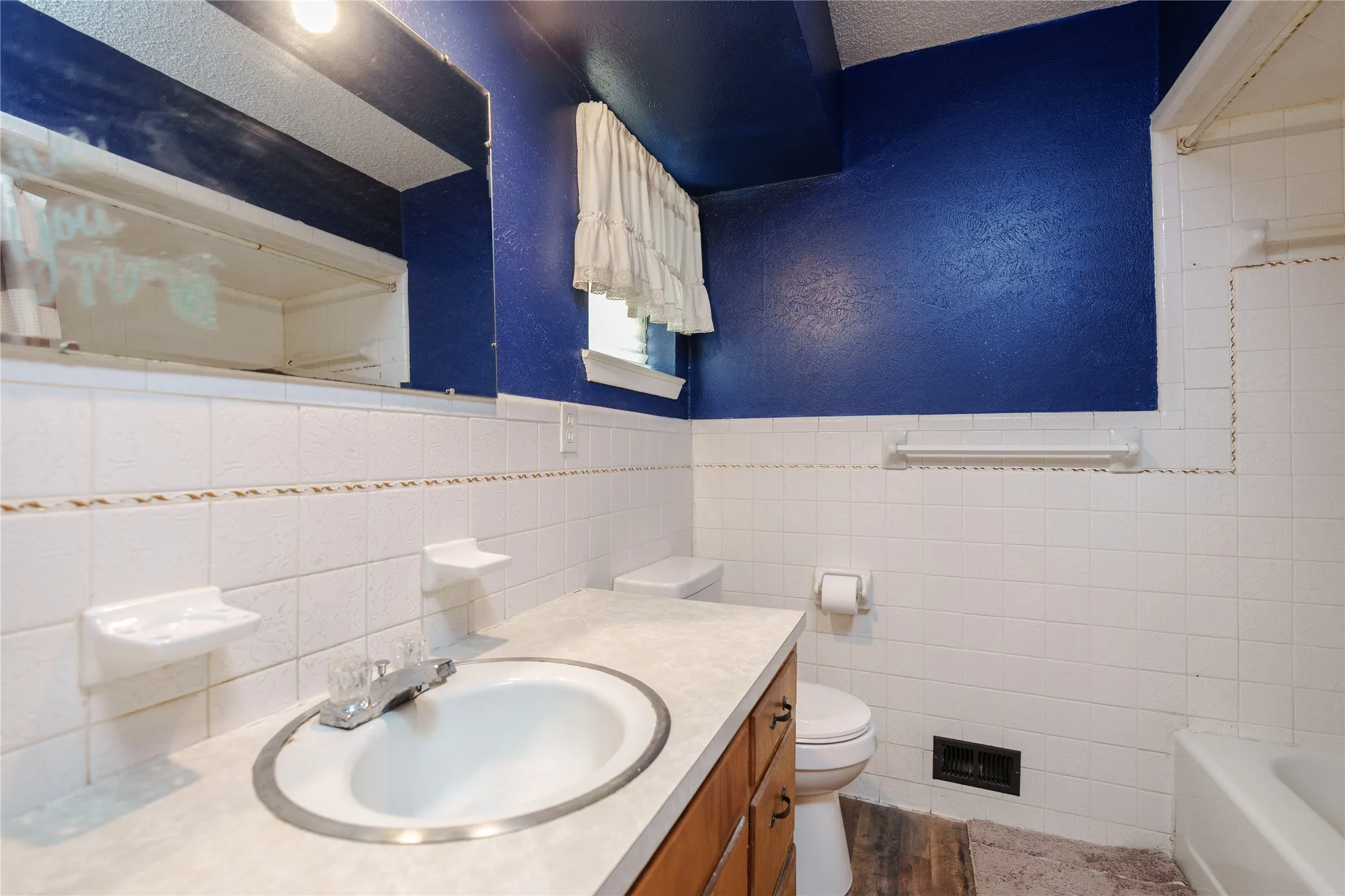 White tiled walls with decorative trim and blue upper walls, vanity with integrated sink and chrome faucet, and a built-in bathtub