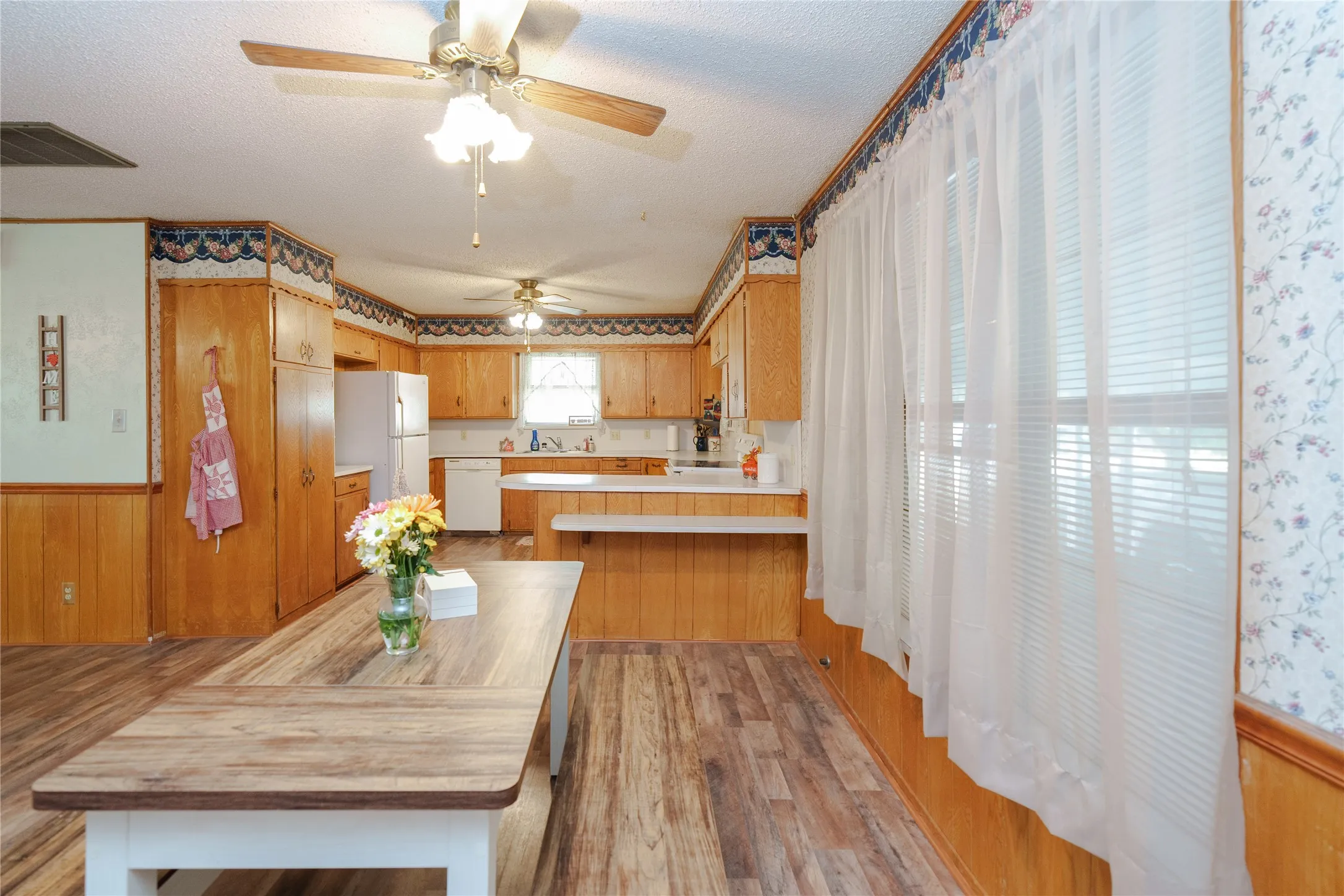 Kitchen featuring wood-finish flooring, wood cabinetry, white appliances, and a built-in breakfast bar