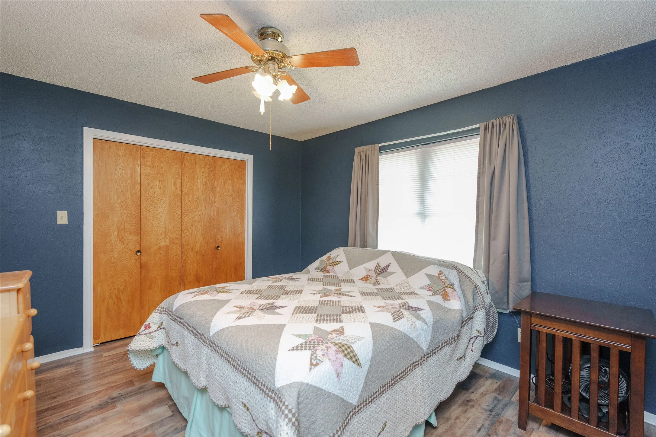 Wood-finish flooring, ceiling fan with integrated lighting, window with blinds, and bi-fold closet doors