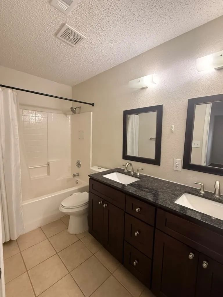 Dual vanity with dark wood-finish cabinetry, integrated rectangular sinks, and dark countertops