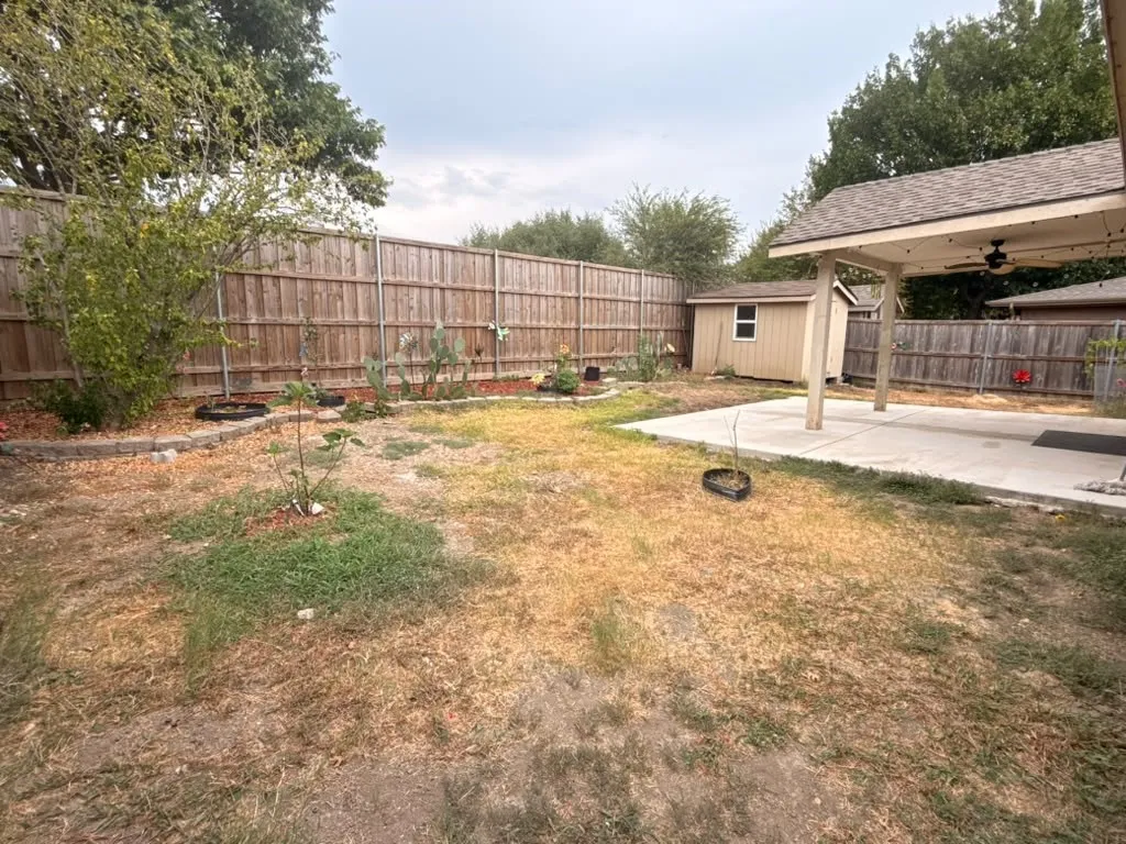 Expansive backyard featuring a covered patio, detached storage shed, wood privacy fencing, and mature perimeter landscaping