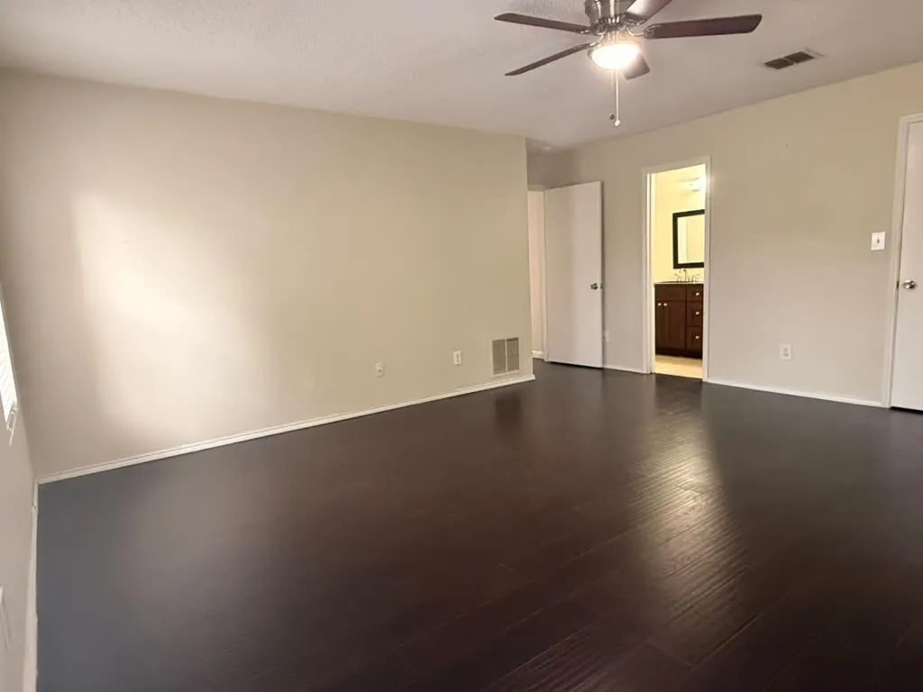Spacious room featuring dark wood-finish flooring, light neutral-toned walls, and a ceiling fan with integrated lighting