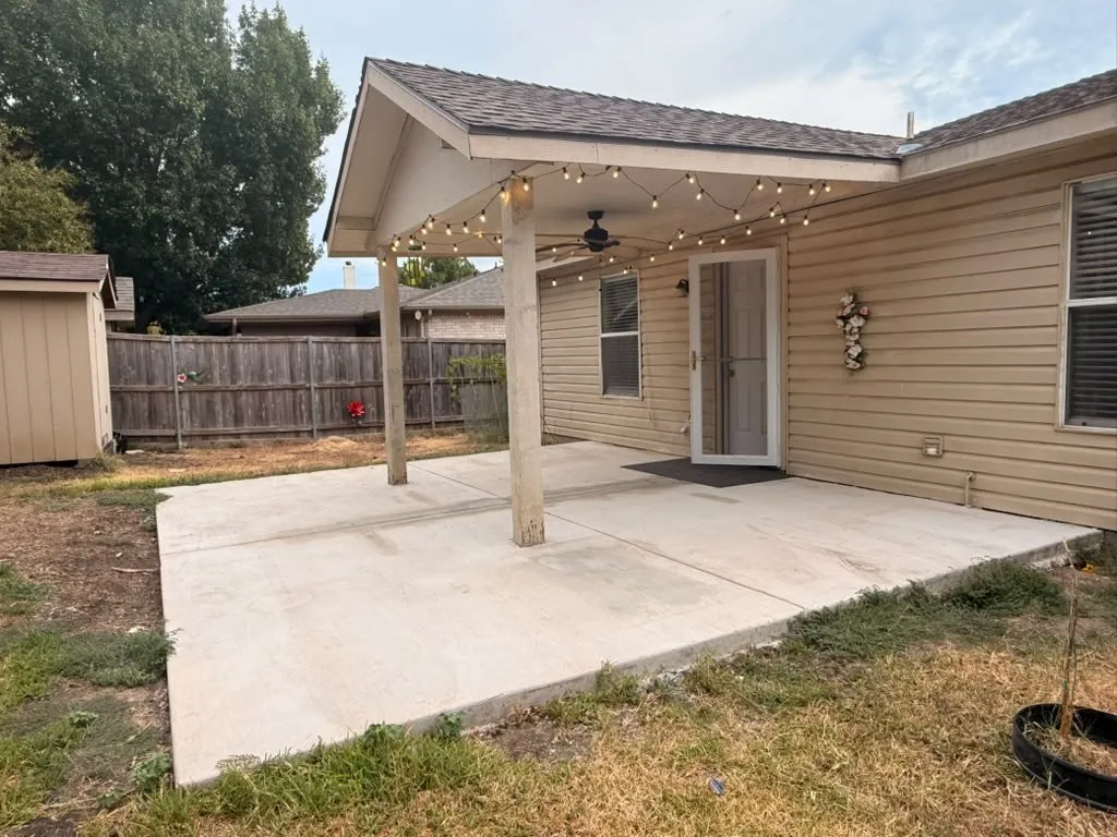 Covered concrete patio with overhead string lighting, built-in ceiling fan, and access to the interior
