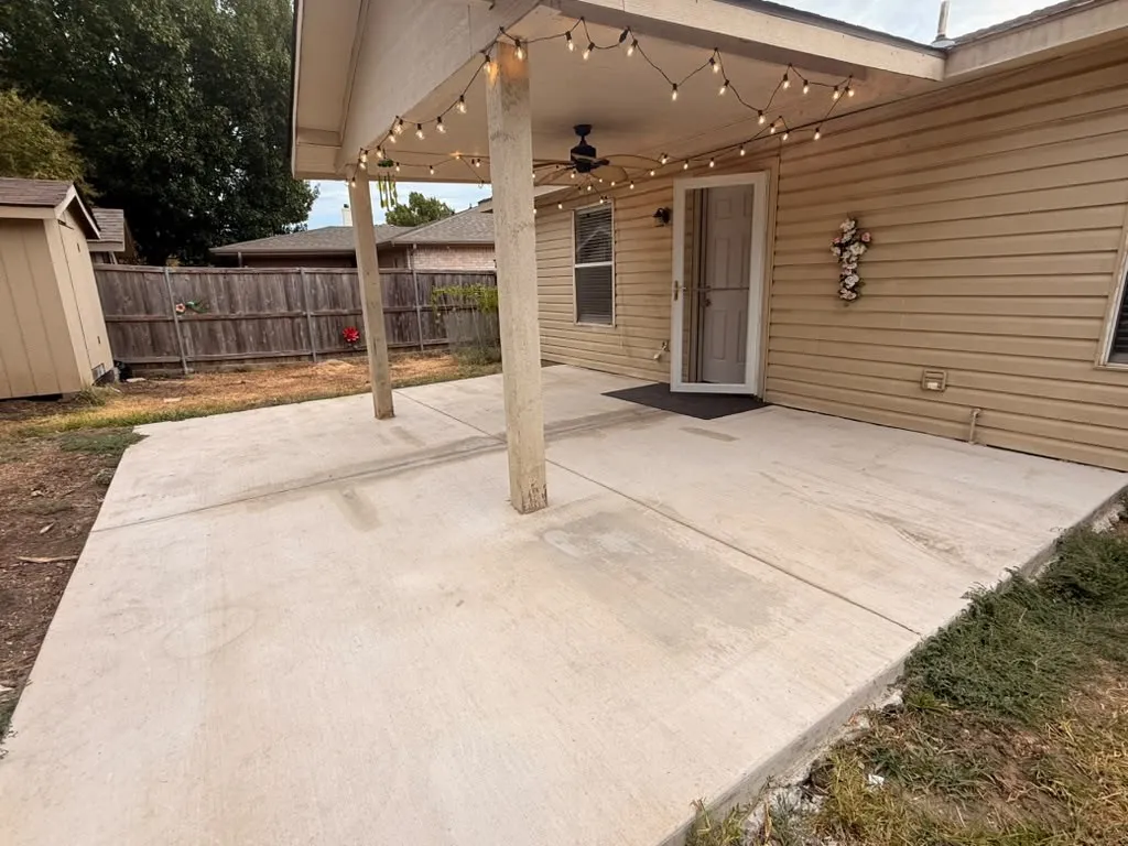 Expansive concrete patio featuring a covered area with a ceiling fan, durable vinyl siding, and a privacy fence