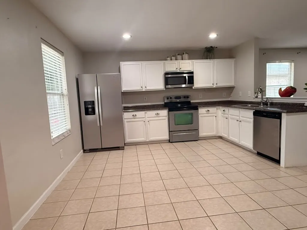 Spacious kitchen featuring white cabinetry, dark countertops, stainless steel appliances, and tile flooring