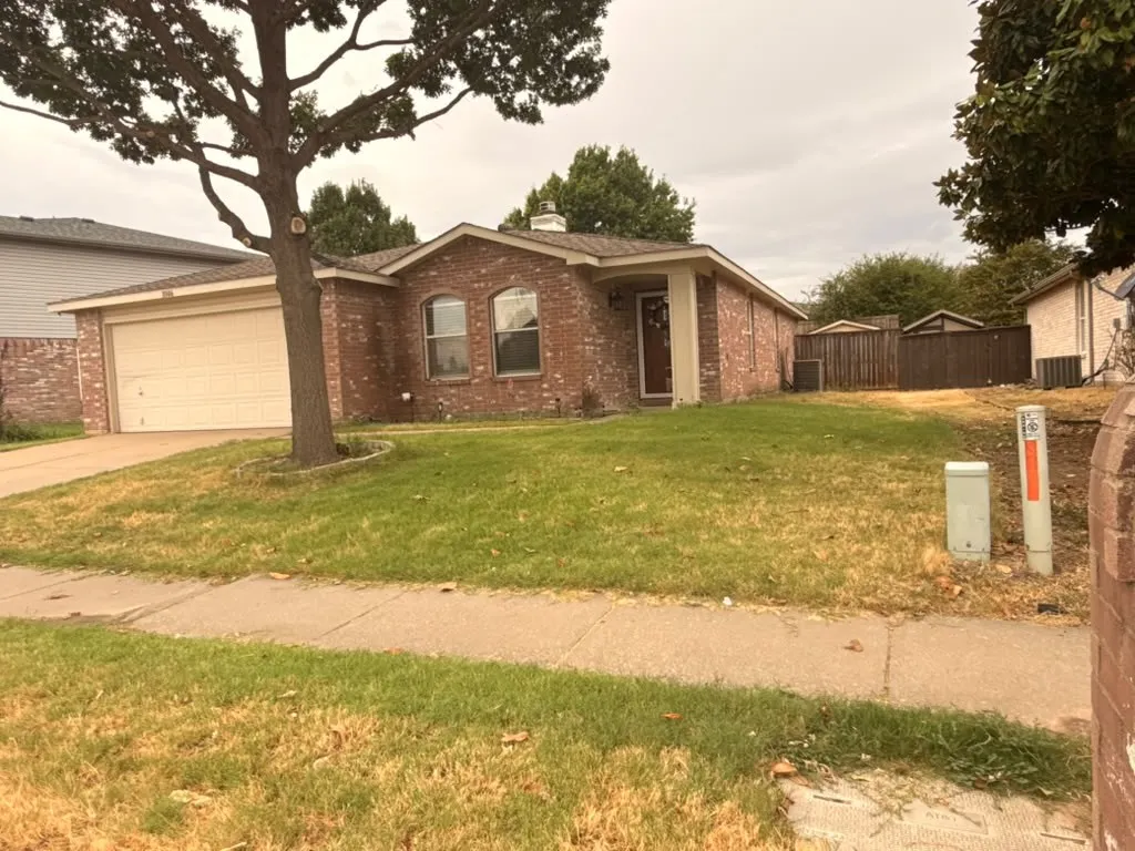 Brick exterior, arched windows, attached garage, covered entryway, and mature tree