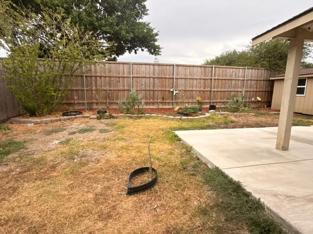 Backyard featuring a privacy fence, concrete patio, garden beds with stone edging, and mature plantings