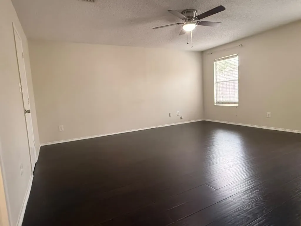 Spacious room featuring dark wood-finish flooring, neutral wall tones, and a ceiling fan with integrated lighting