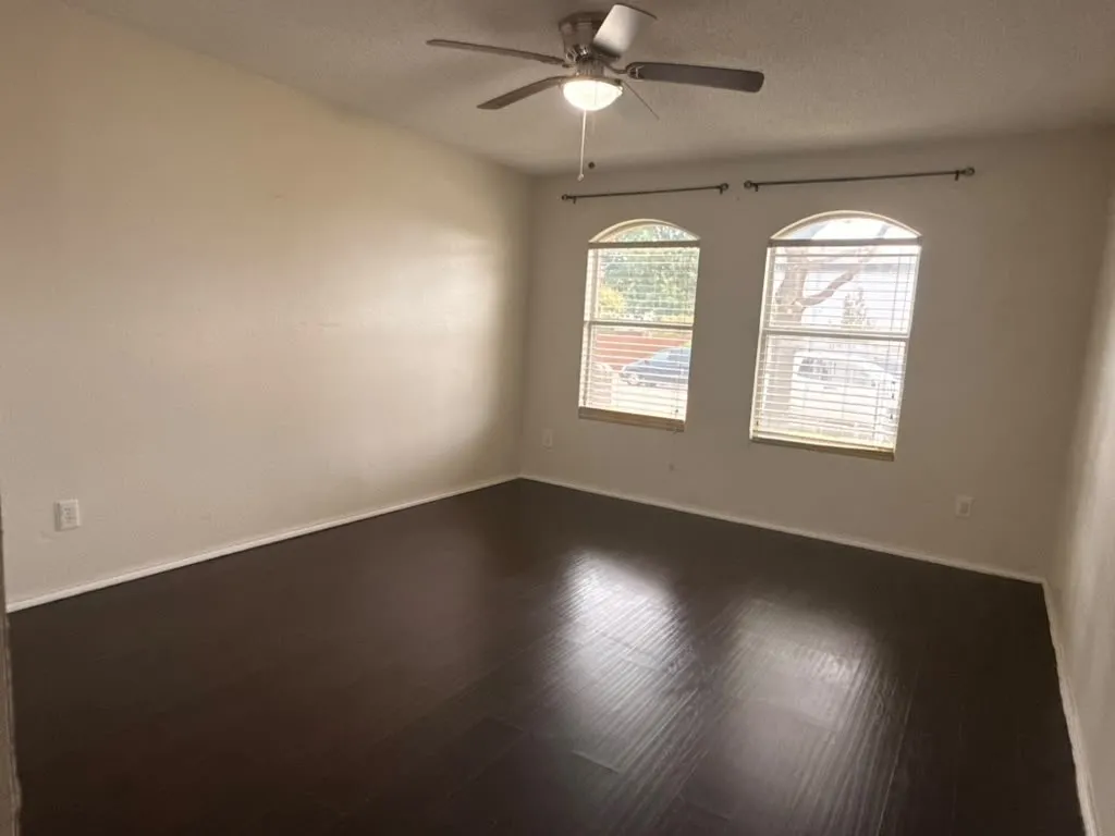Spacious interior with dark wood-finish flooring, light-toned walls, and a ceiling fan