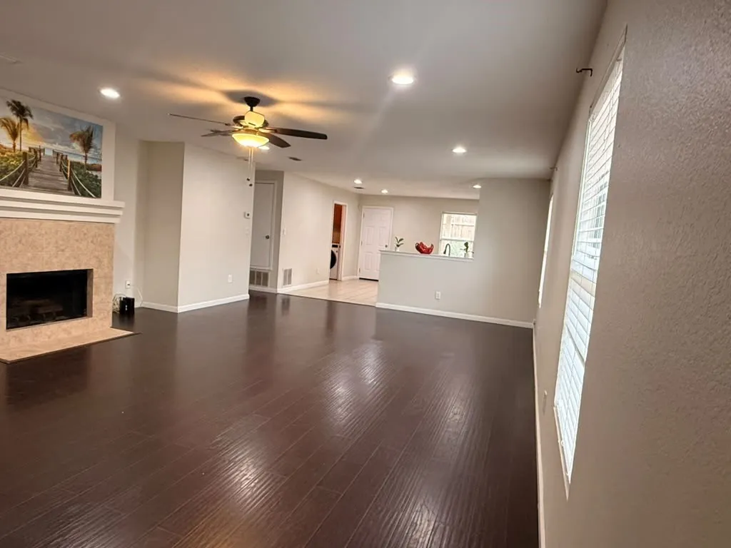 Spacious room featuring dark wood-finish flooring, a fireplace with a light-toned surround, recessed lighting, and a ceiling fan