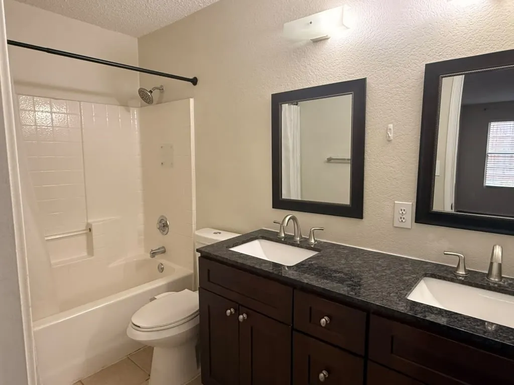 Double vanity with undermount sinks, speckled dark countertop, and dark wood-finish cabinetry