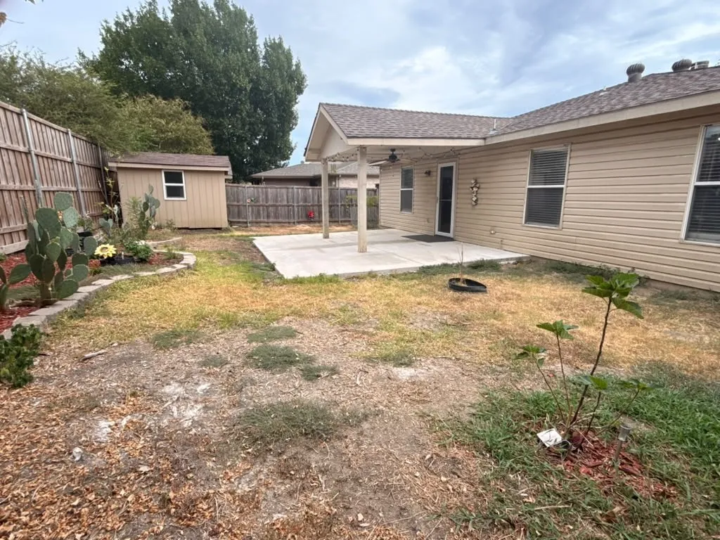 Backyard featuring a covered patio, concrete slab, wood privacy fencing, and a storage shed