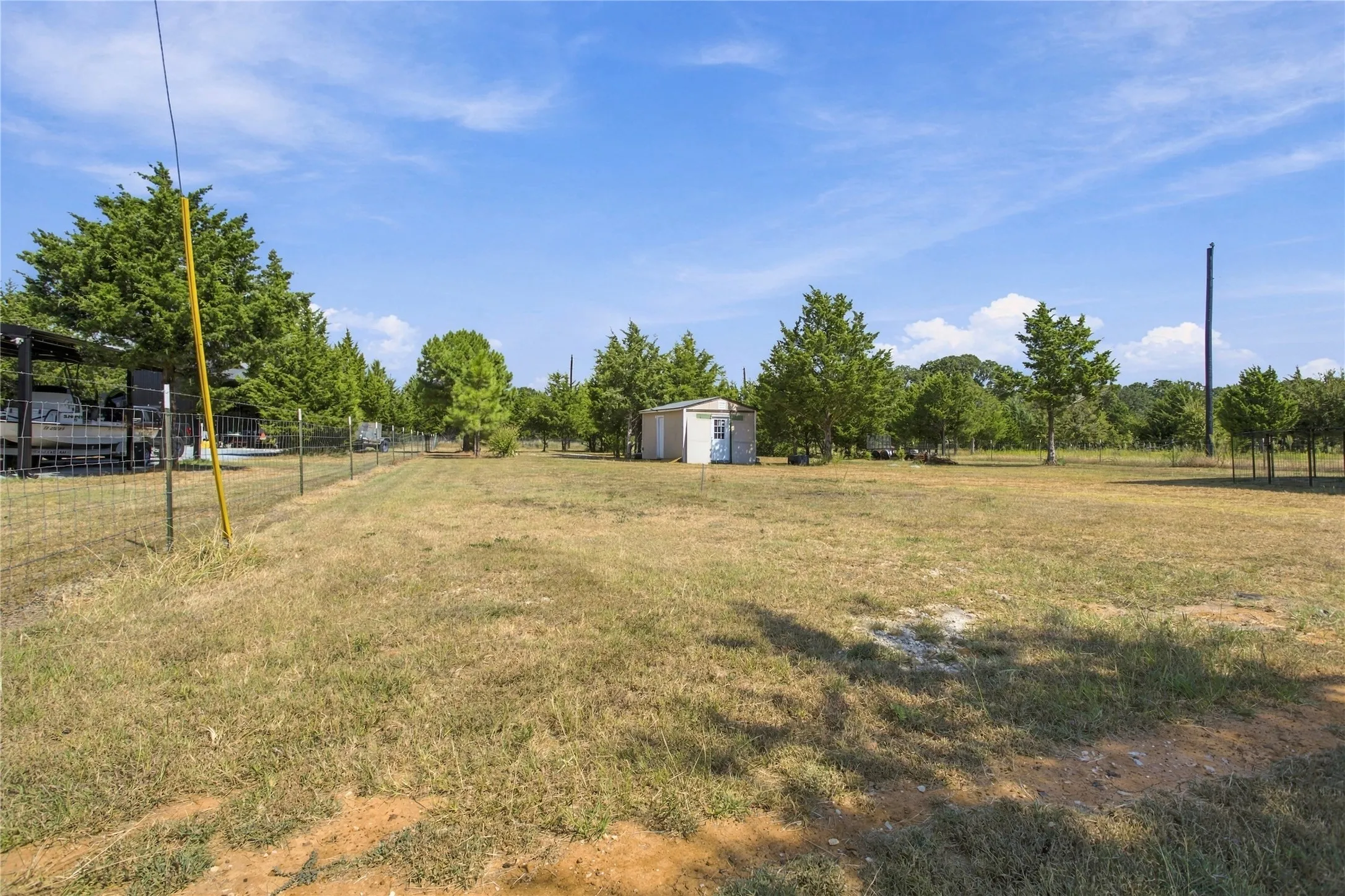 Expansive open lot featuring mature trees, a detached storage shed, and perimeter fencing