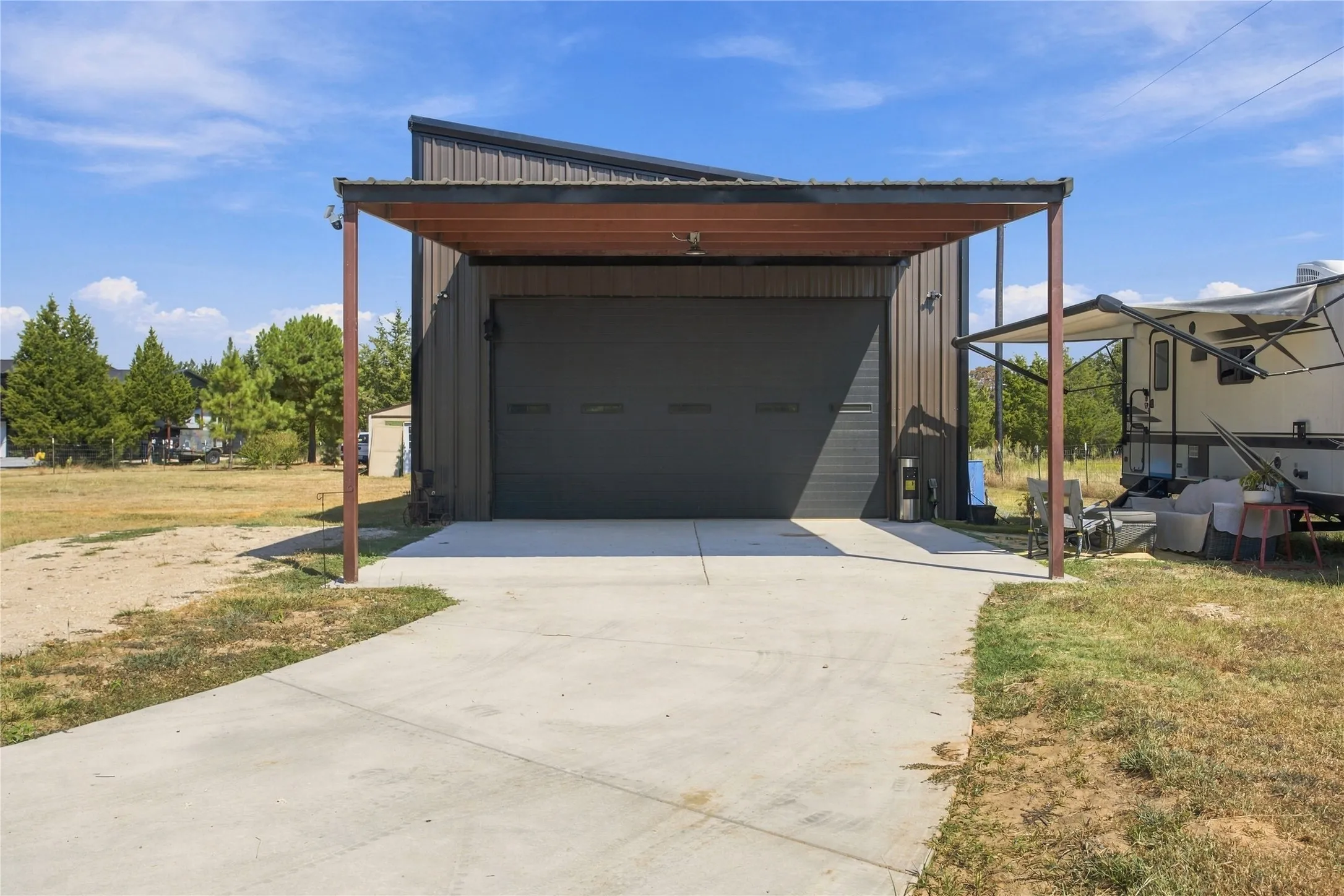 Metal construction garage with a large roll-up door, an attached carport, and a concrete driveway