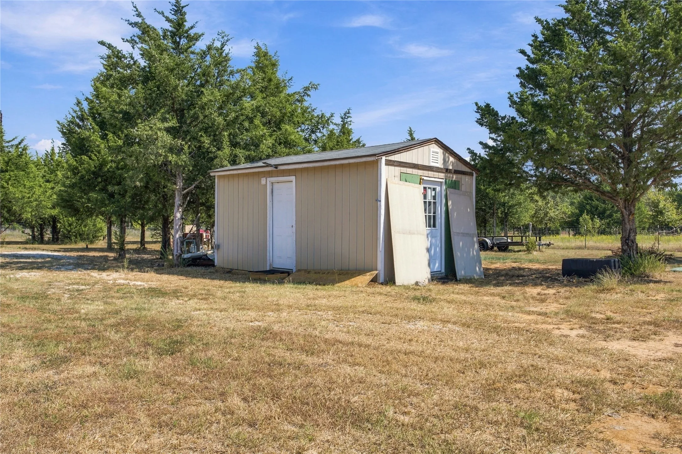 Shed with beige siding, a gable roof, and a white entry door