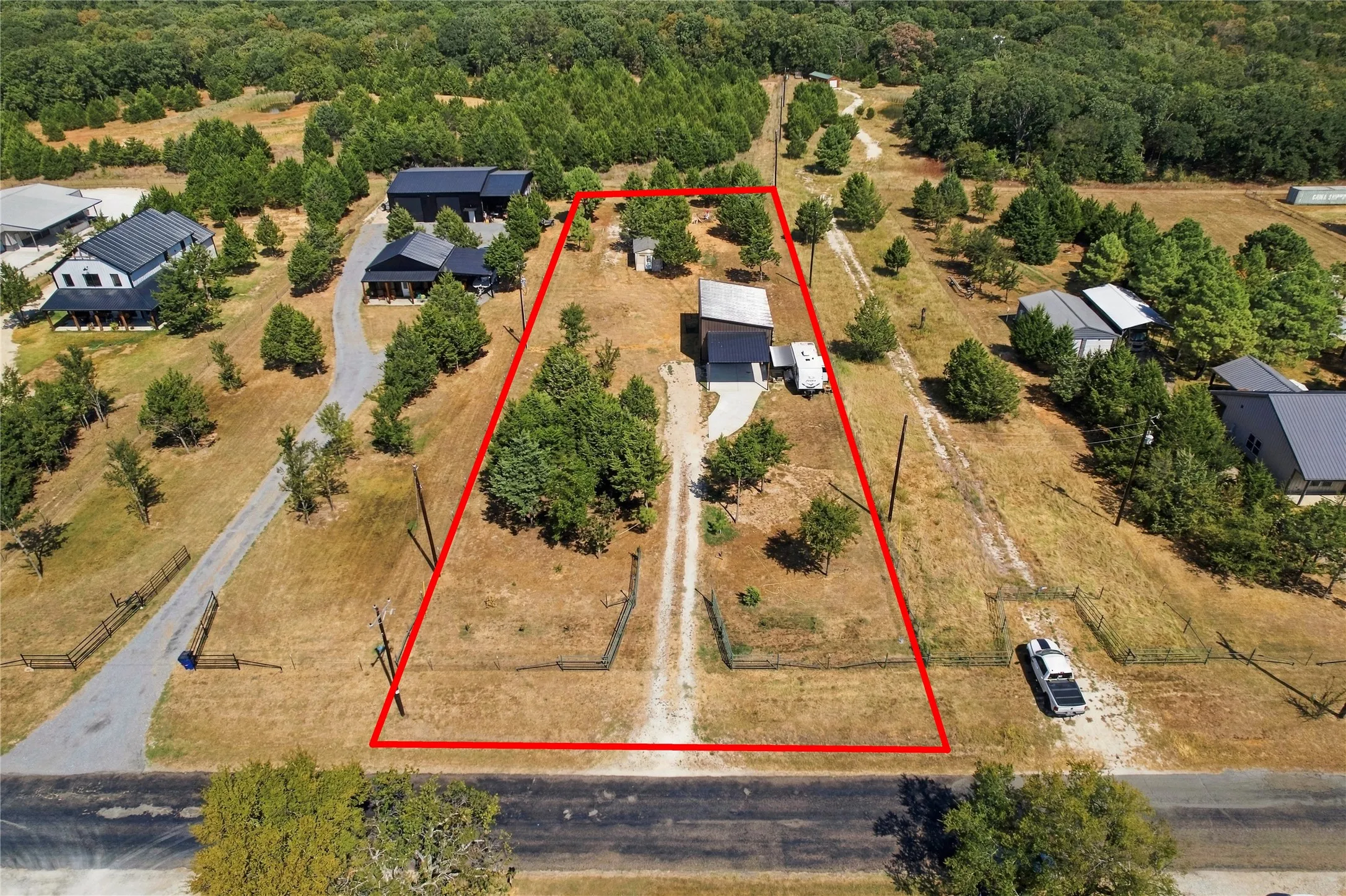 Expansive lot featuring a single-story residence with a light-colored roof, a paved driveway, and mature trees