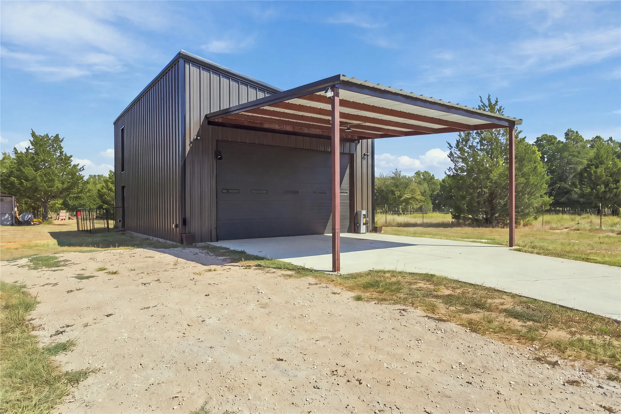 Metal siding exterior featuring a covered carport, concrete driveway, and large roll-up door