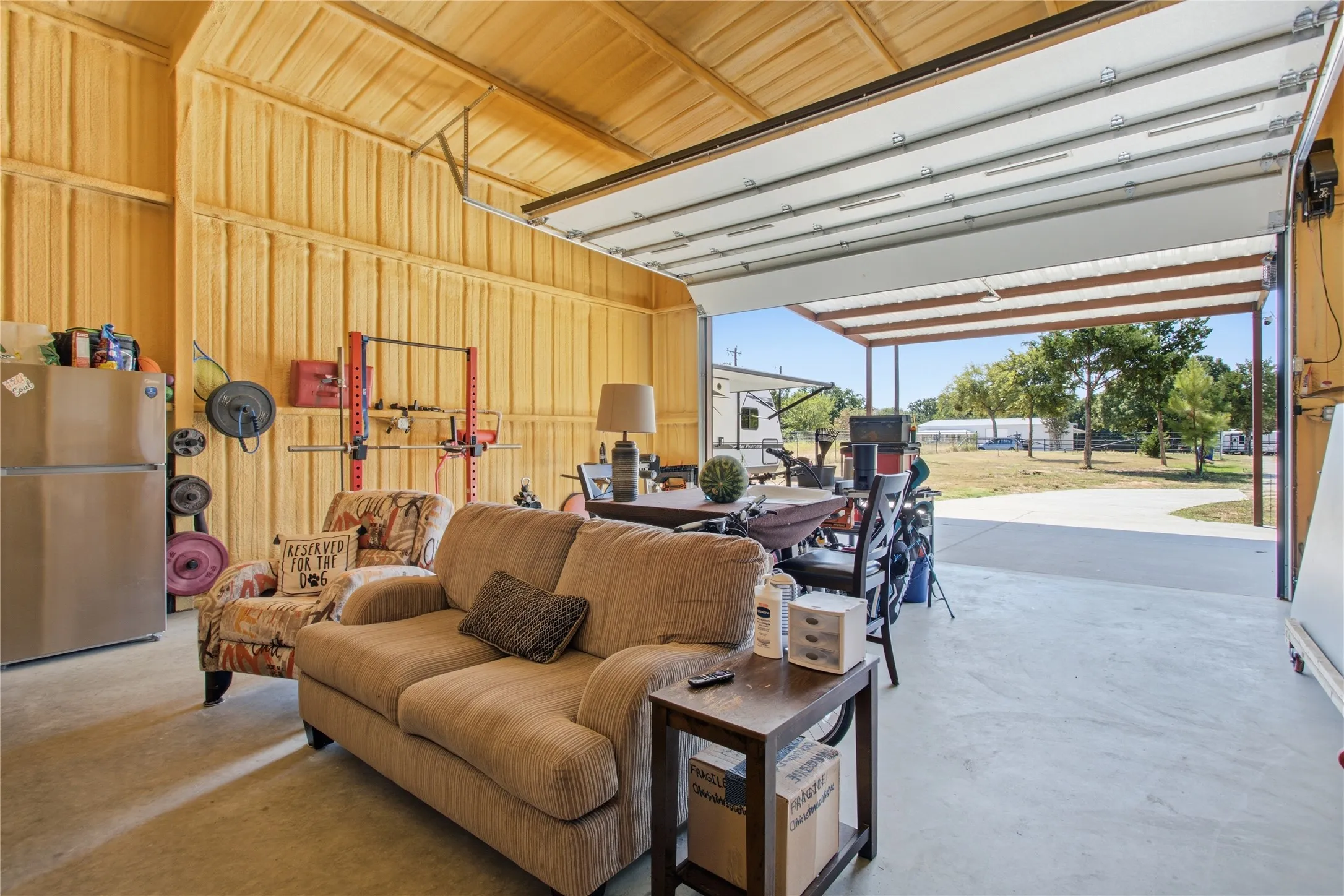 Spacious open structure featuring a roll-up garage door, exposed wood-finish ceiling, and concrete flooring