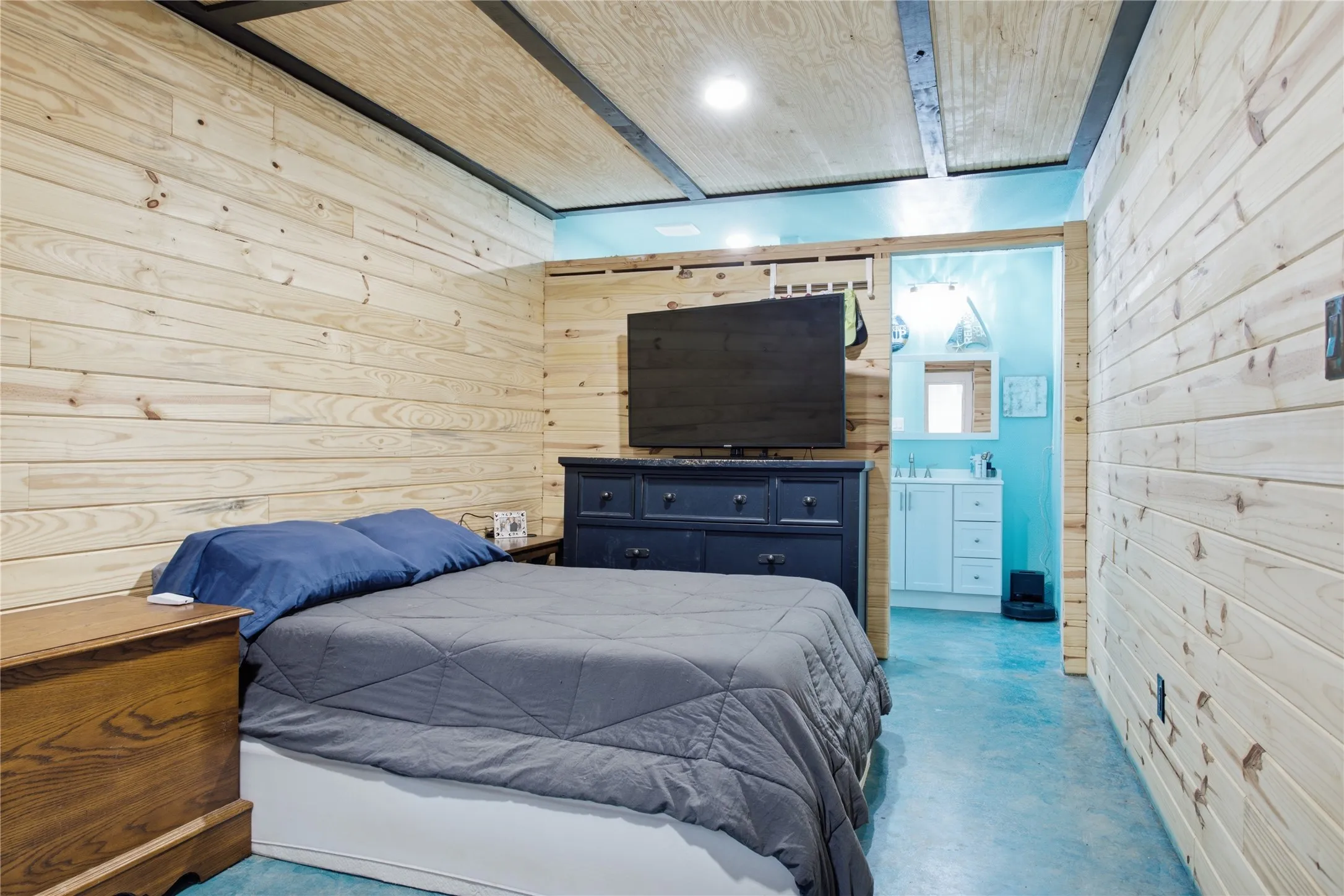 Wood-paneled walls and ceiling with exposed beam accents, recessed lighting, and an adjacent bathroom with a white vanity and mirror