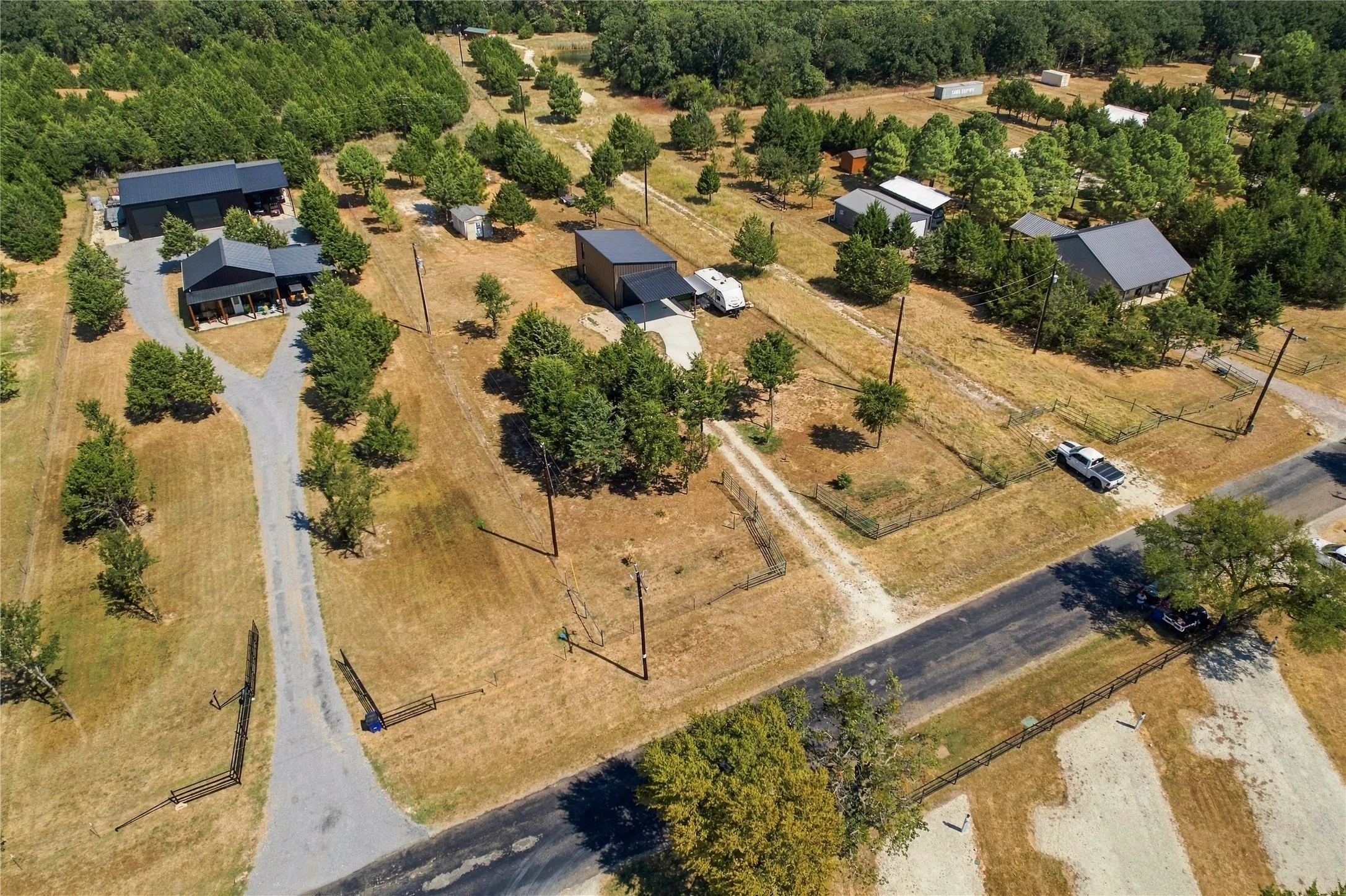Expansive property featuring multiple residential structures, detached outbuildings, a paved road, and mature trees