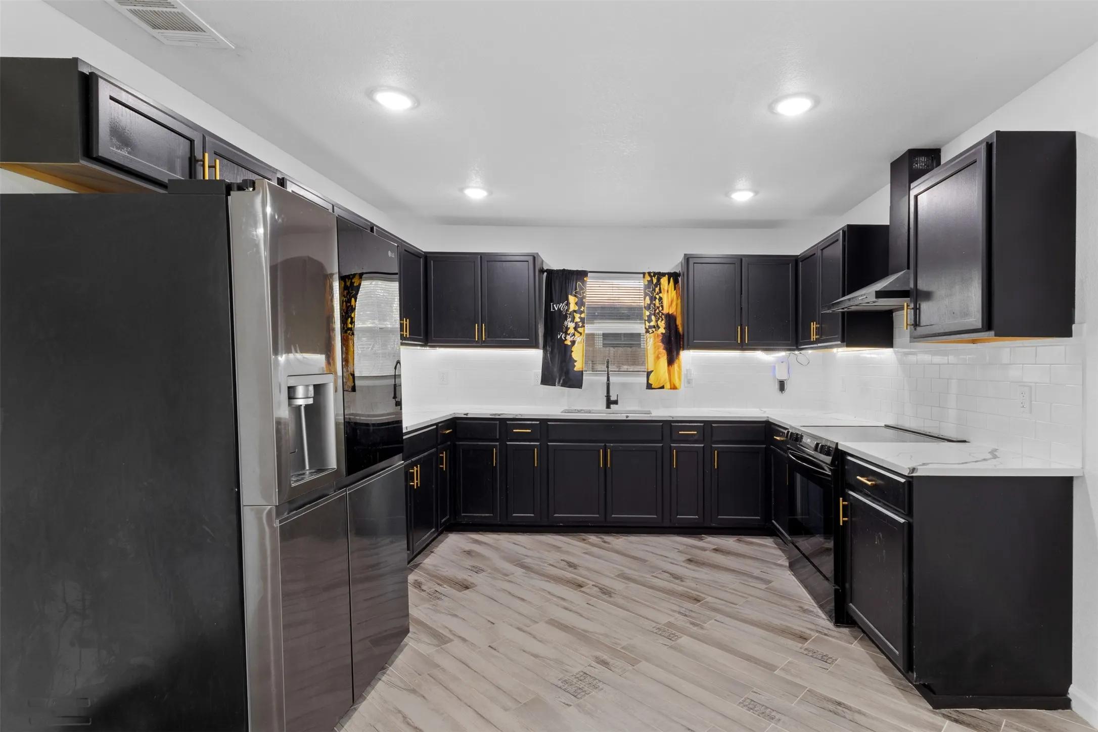Contemporary kitchen featuring dark cabinetry with gold-tone hardware, white countertops, white subway tile backsplash, and wood-finish flooring