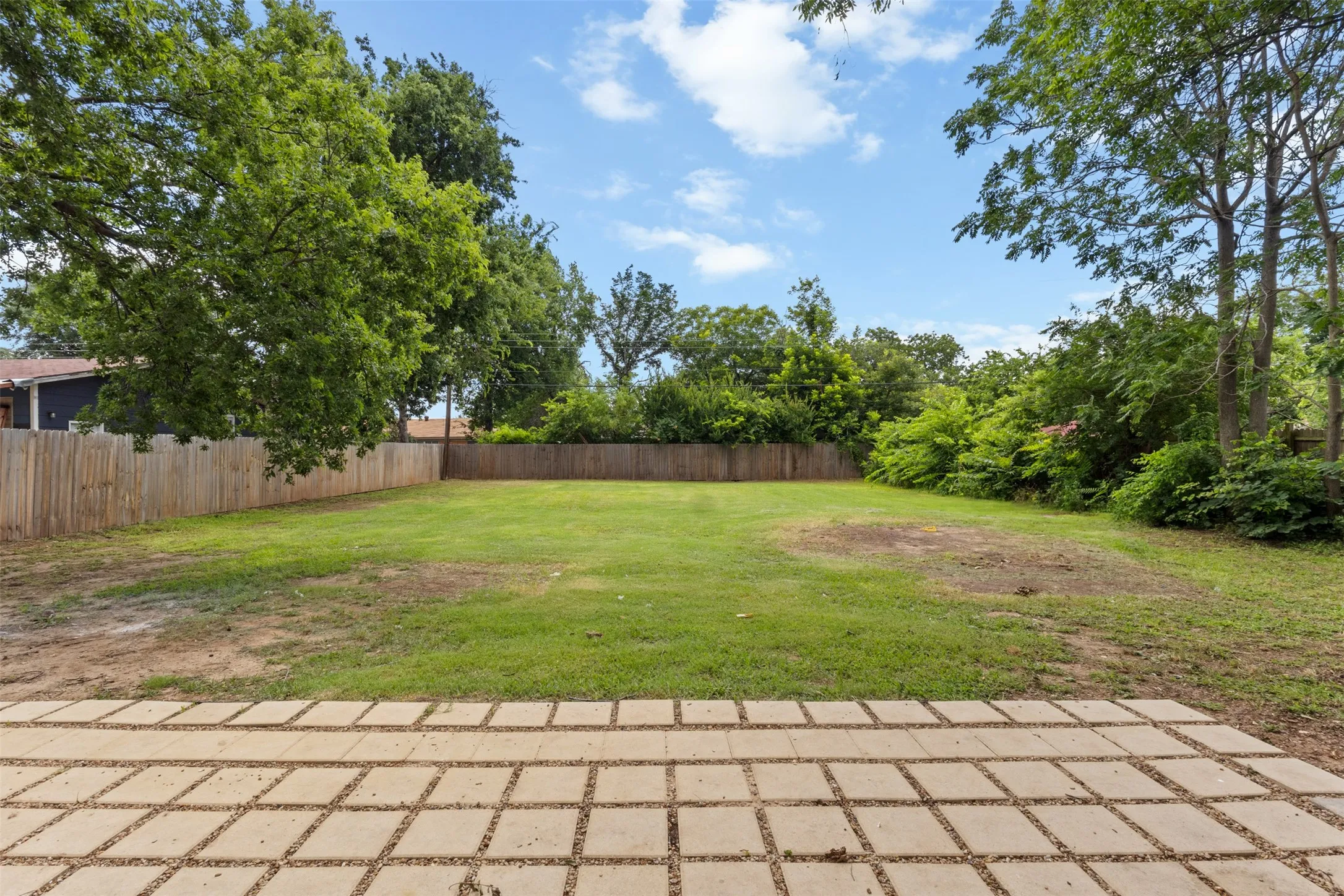 Expansive backyard featuring a large grass area, mature trees, and a wooden privacy fence