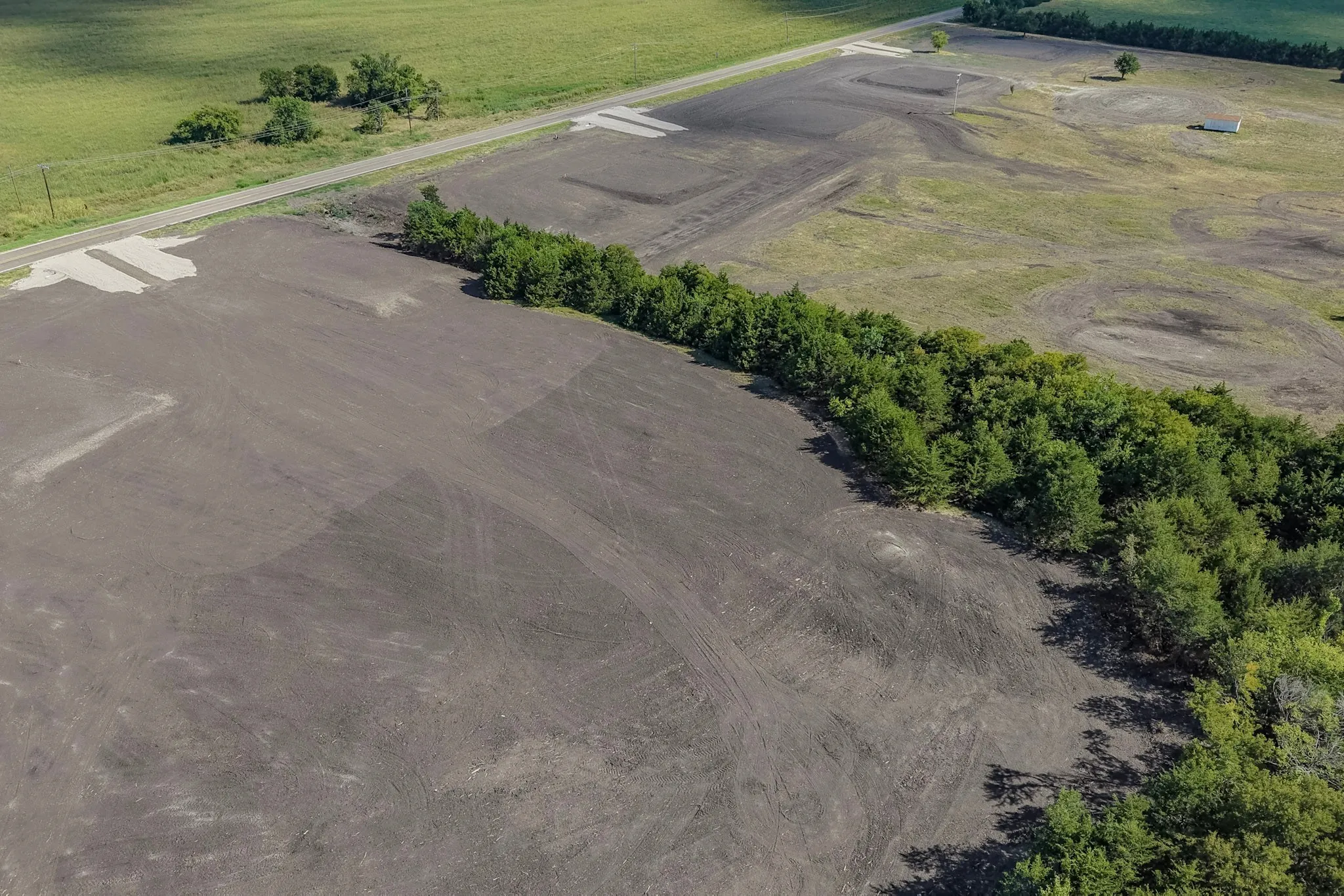 Expansive cleared land featuring a tree line and adjacent roadway