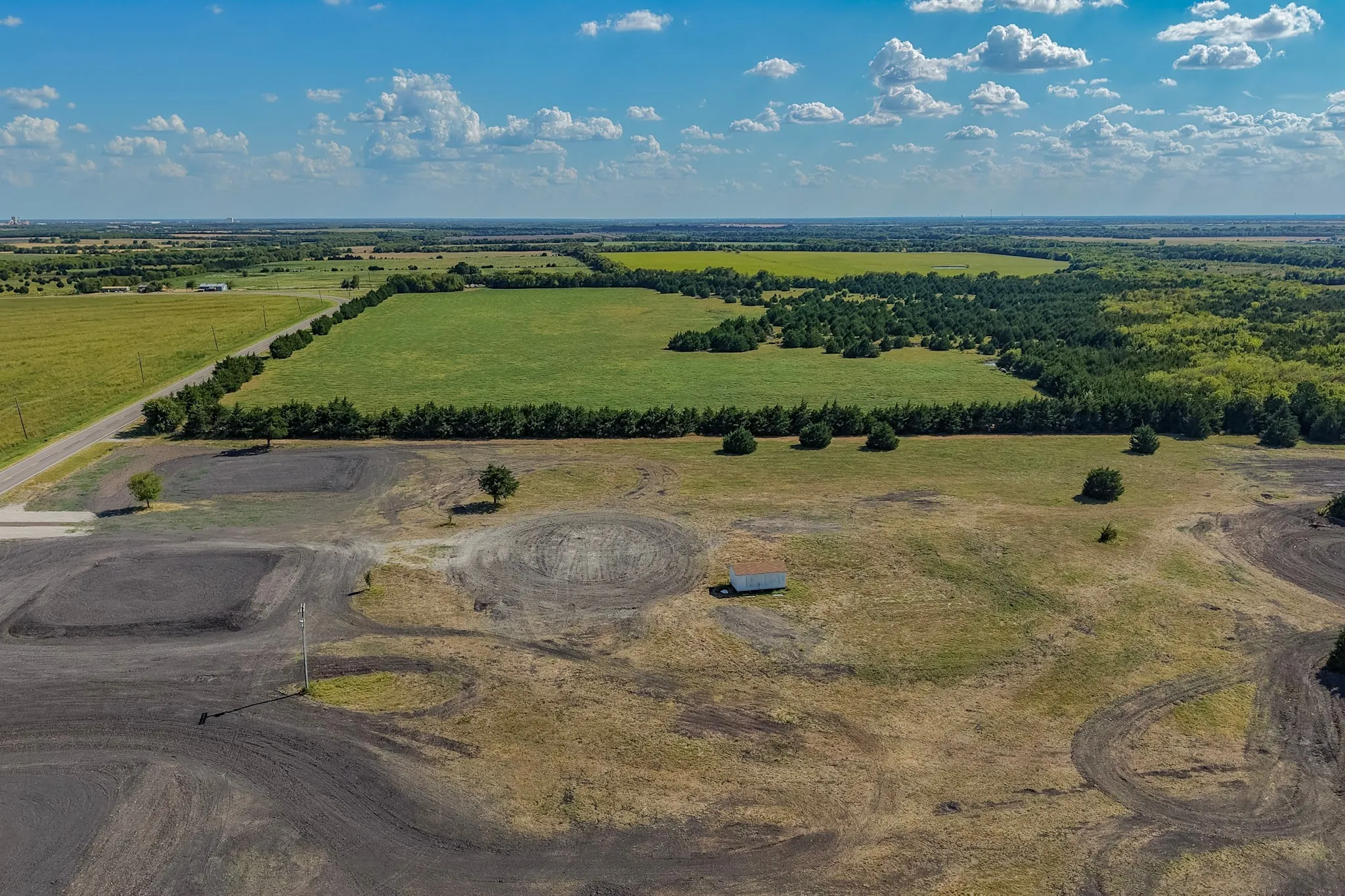 Expansive undeveloped land featuring varied terrain, a small outbuilding, and mature trees