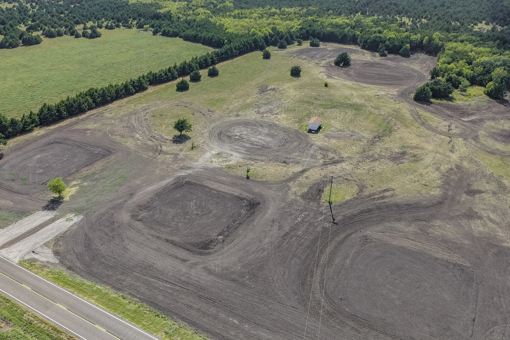 Expansive undeveloped land featuring a cleared building site, mature trees, and a paved road frontage