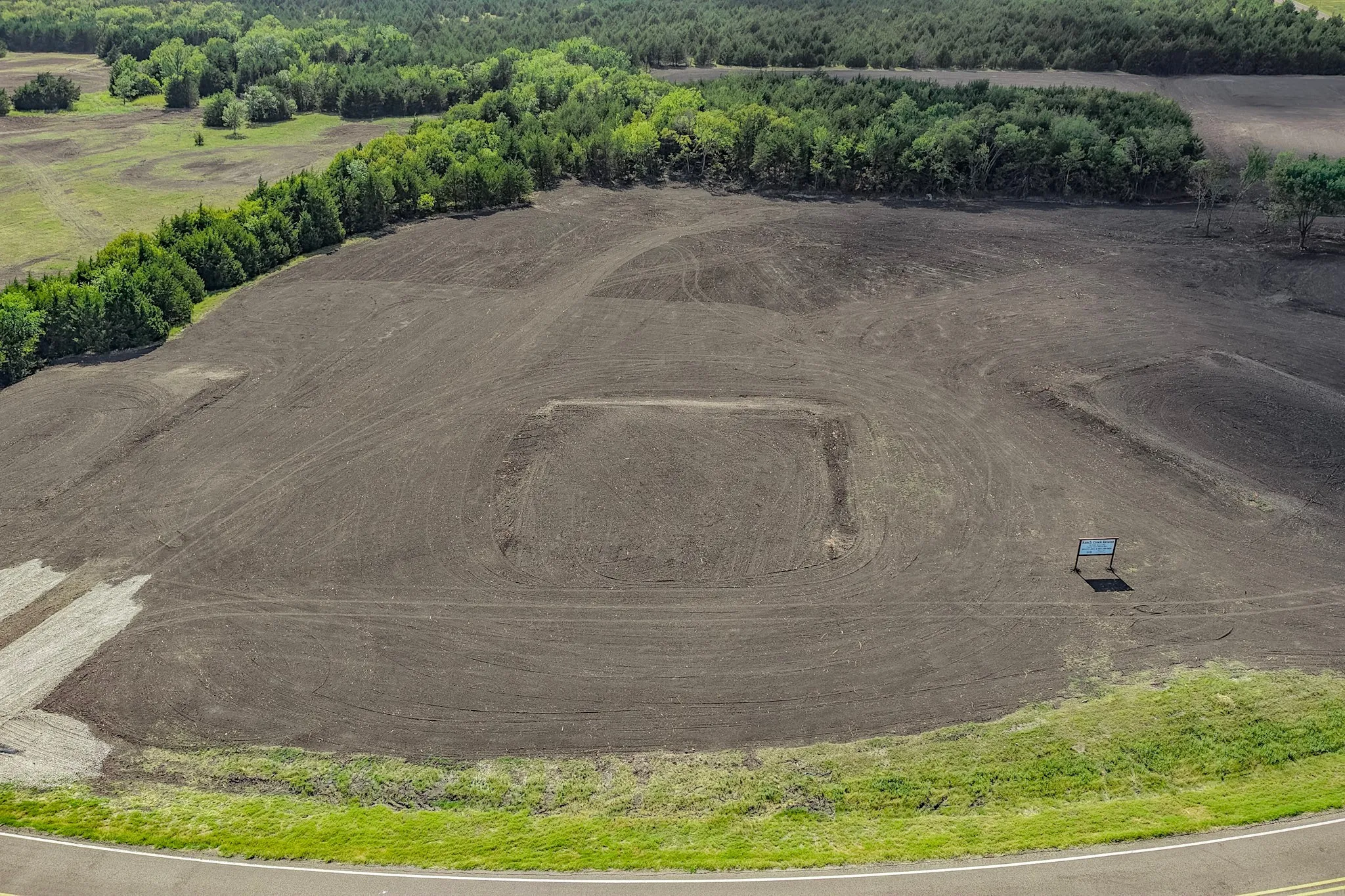 Expansive open land featuring cultivated soil and a perimeter of mature trees