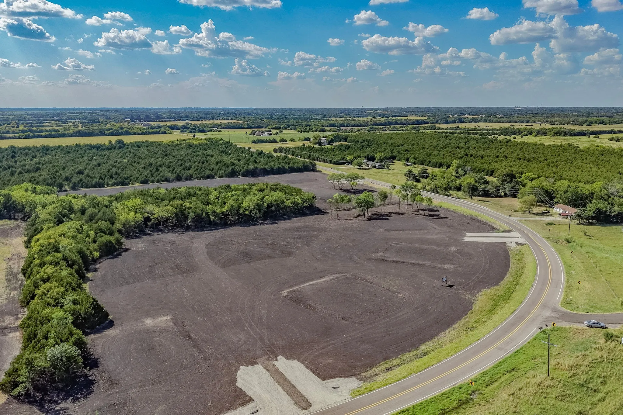 Expansive land parcel with surrounding tree lines, cleared building areas, and direct road frontage