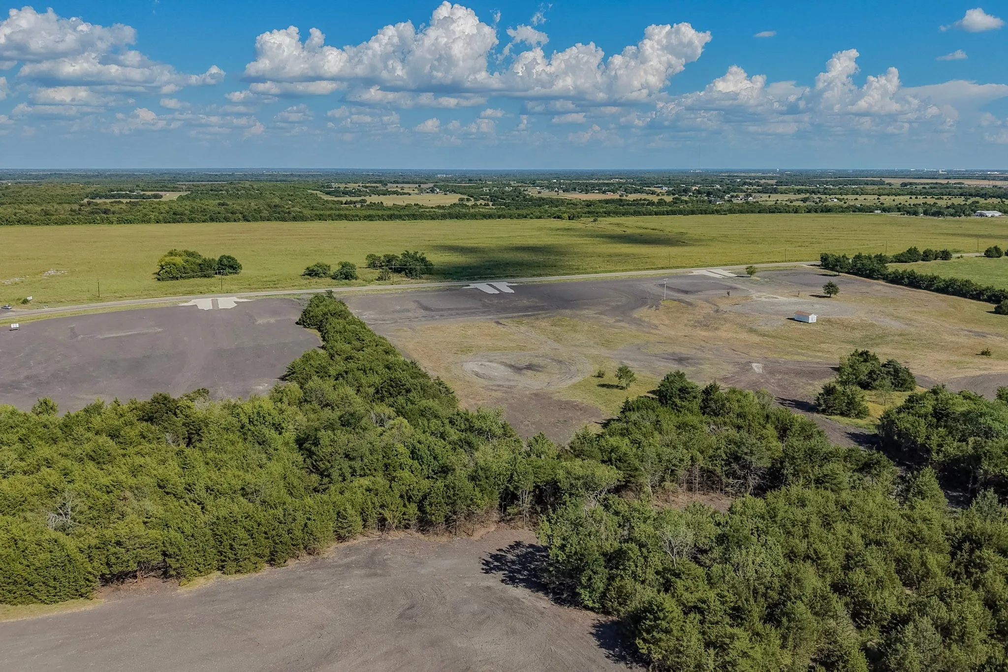 Expansive land parcel featuring partial tree coverage, open fields, and distinct dark and light ground areas
