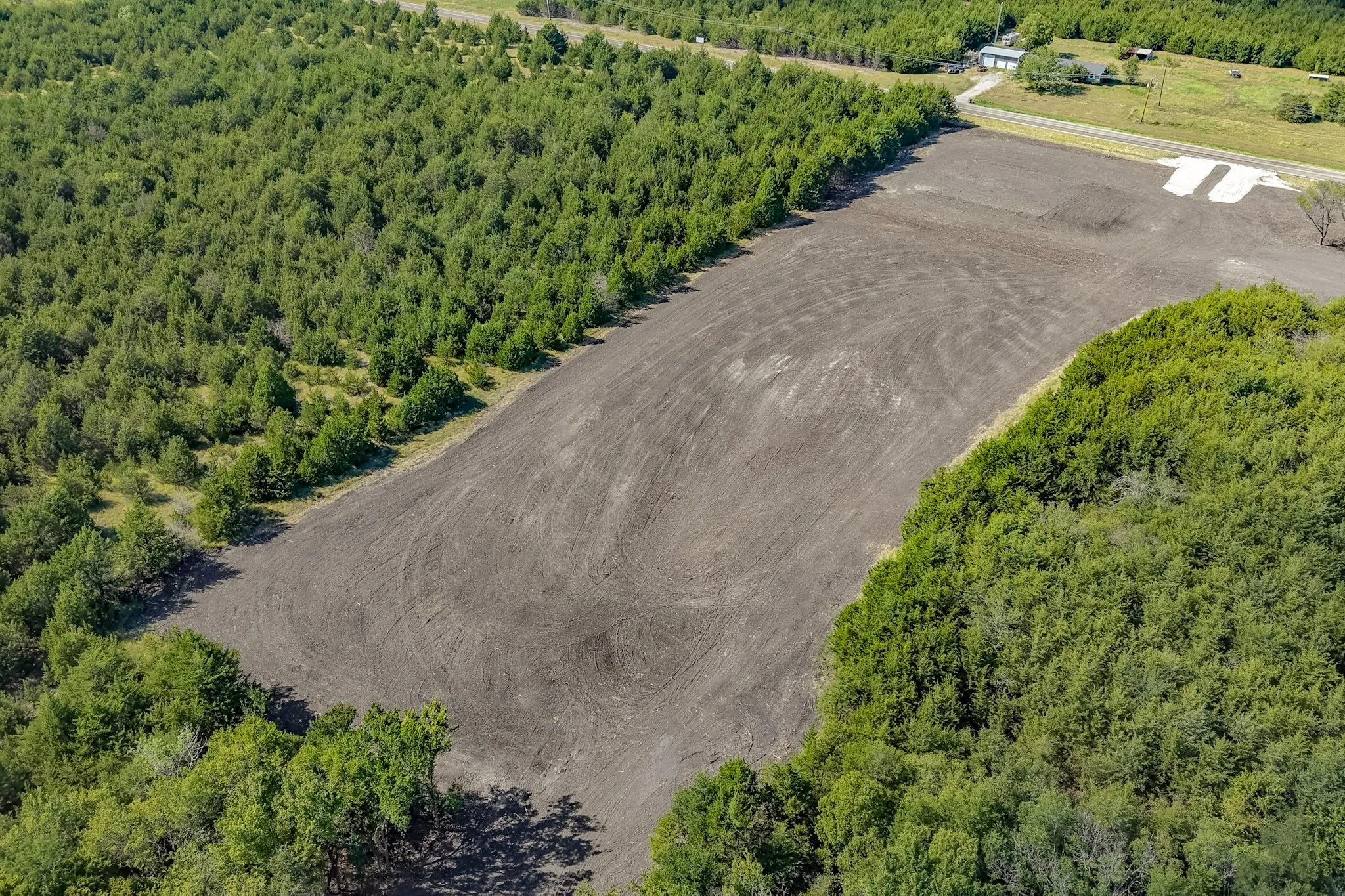 Expansive cleared lot with surrounding mature trees and visible access road