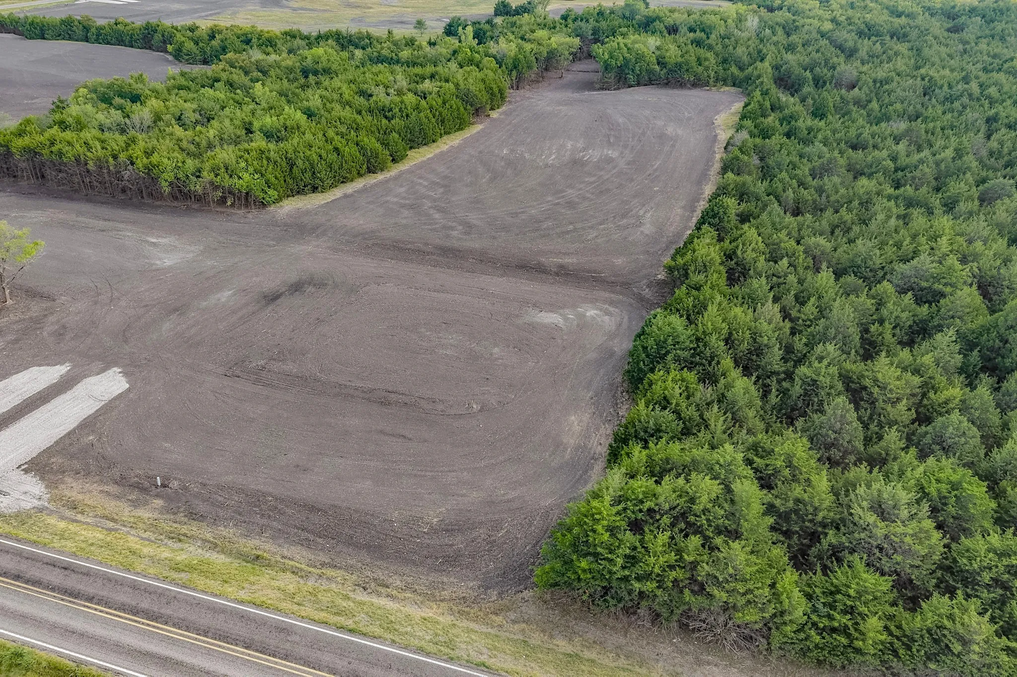 Expansive cleared land bordering mature tree lines and a paved road