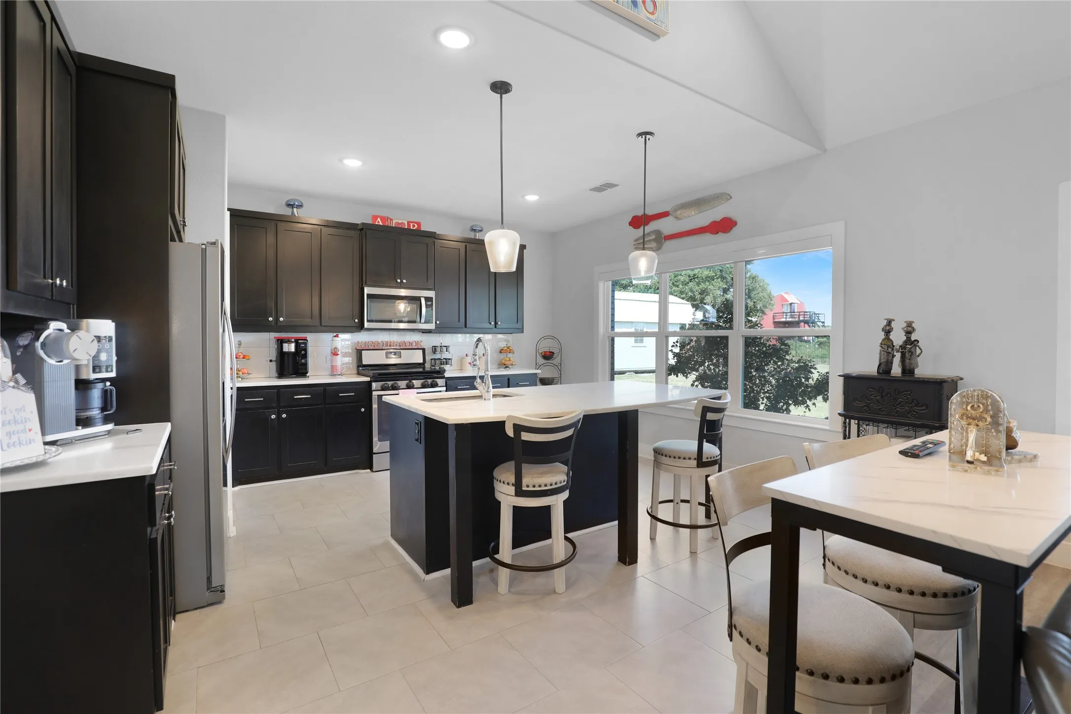 Kitchen featuring dark cabinetry, white countertops, stainless steel appliances, a center island with seating, and light-colored flooring