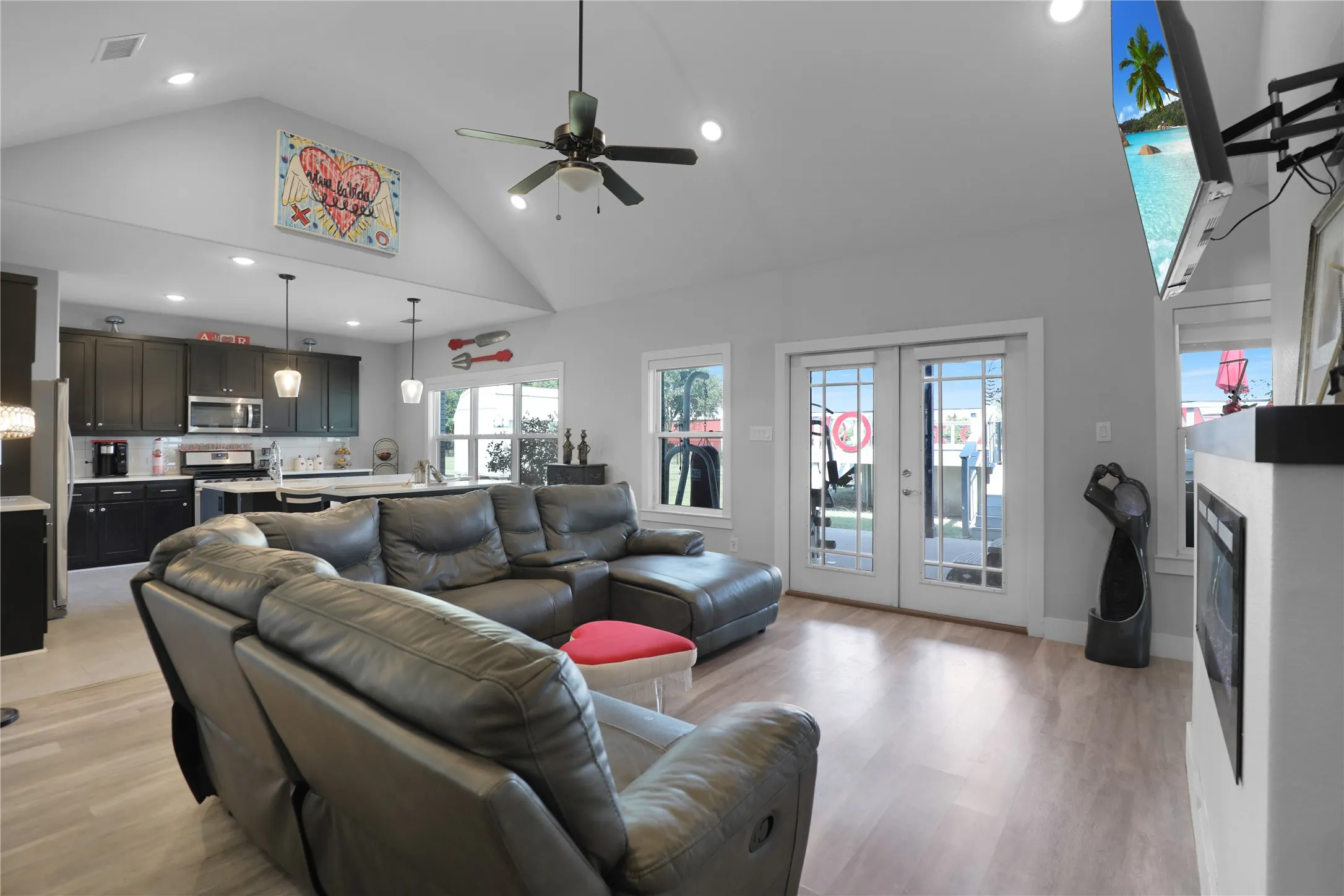 Vaulted ceiling with recessed lighting, wood-finish flooring, white double French doors, dark cabinetry, and a built-in fireplace