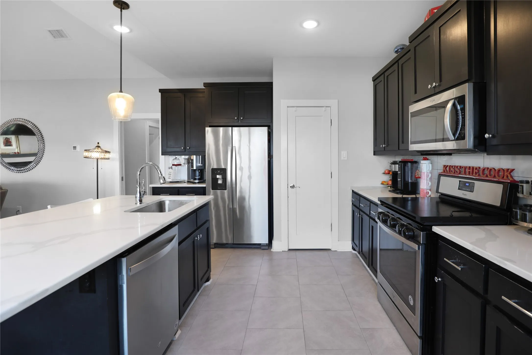Kitchen featuring dark wood cabinetry, stainless steel appliances, a center island with a sink, white countertops, and light-colored tile flooring
