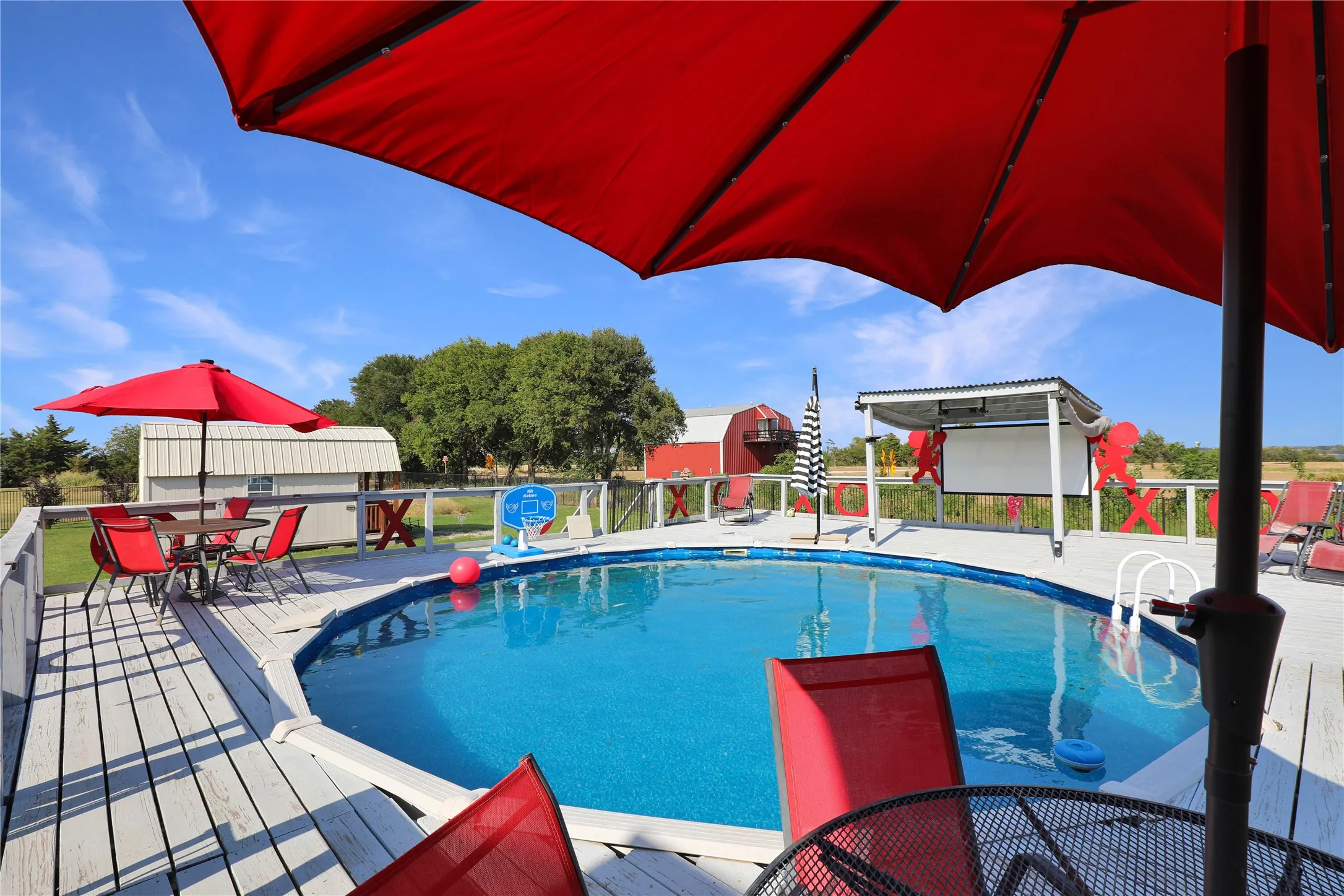 Expansive outdoor decking encircles an above-ground pool, featuring a metal railing and two red patio umbrellas