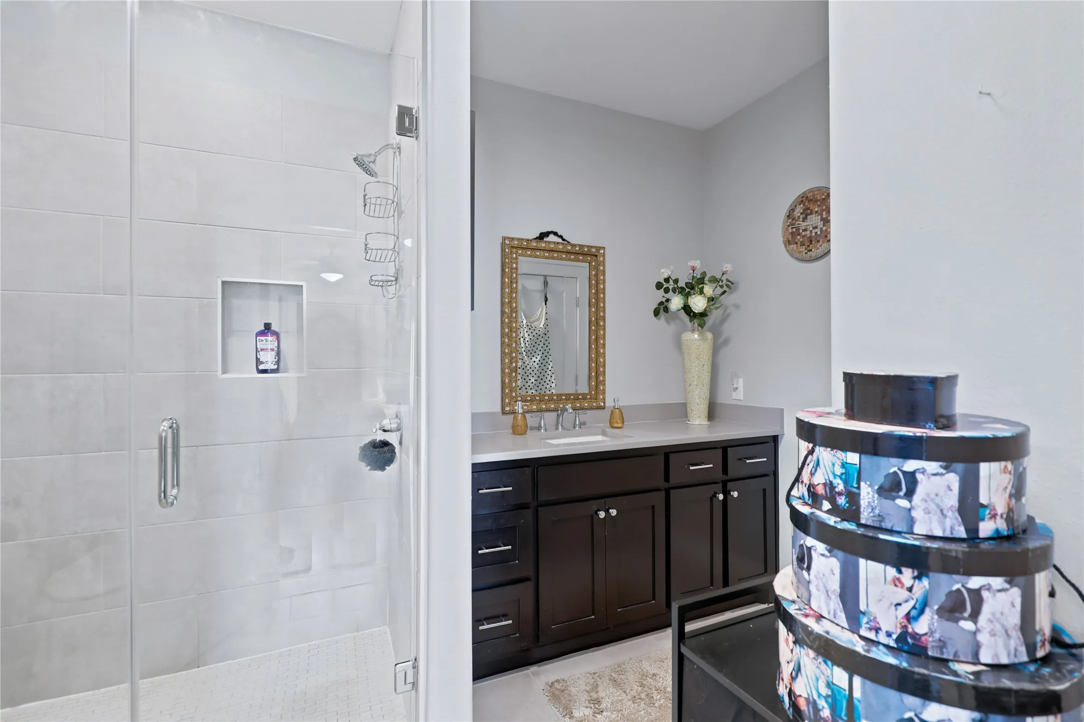 Glass-enclosed shower with a tiled surround, built-in shelving, and a dark wood-finish vanity with a light-toned countertop