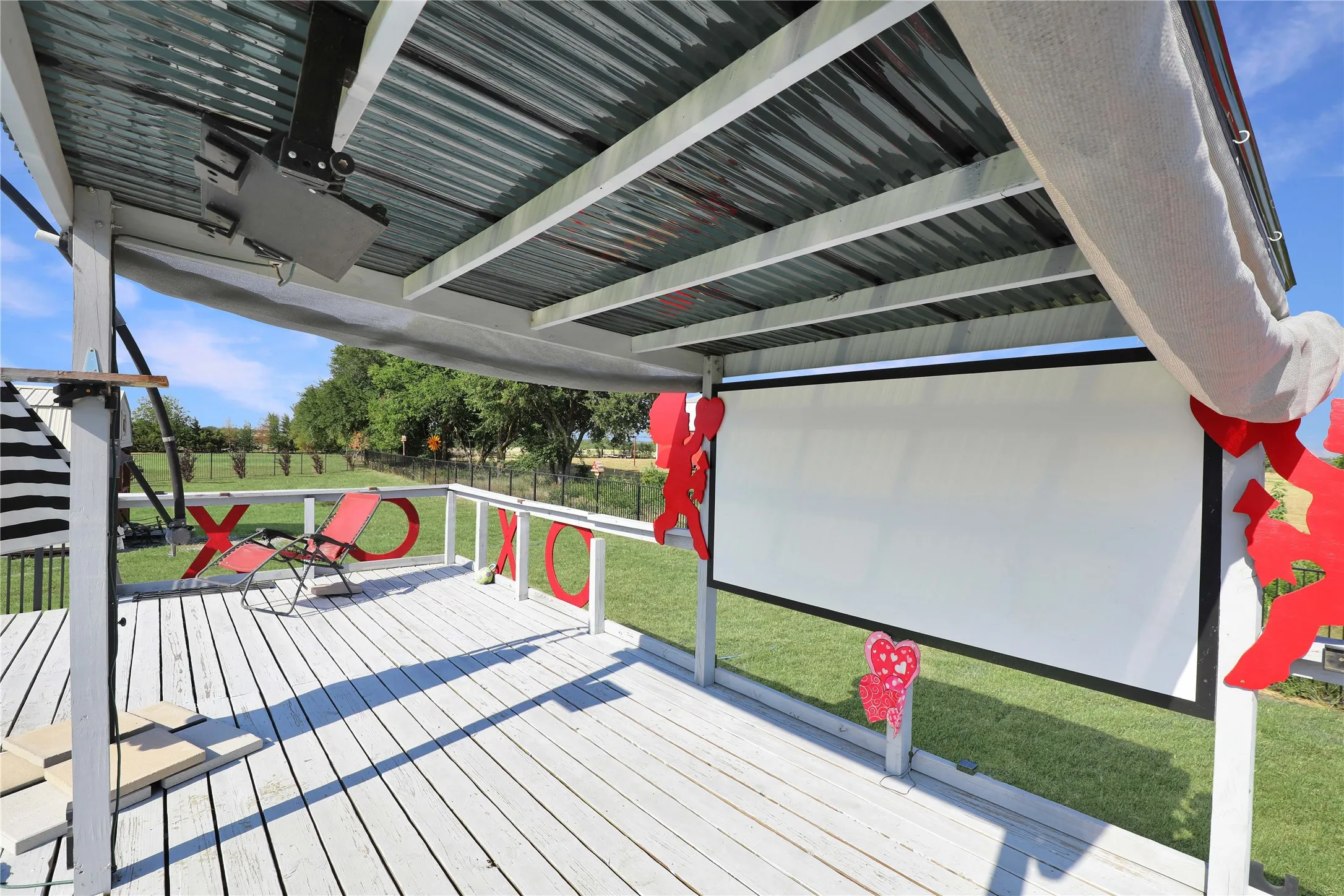 Outdoor covered deck featuring a mounted projector, pull-down screen, and corrugated metal roof