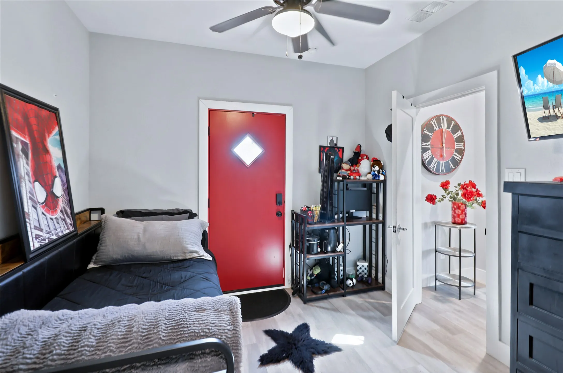 Light-toned wood-finish flooring, ceiling fan with integrated lighting, a red door with a diamond-shaped window, and white interior doors