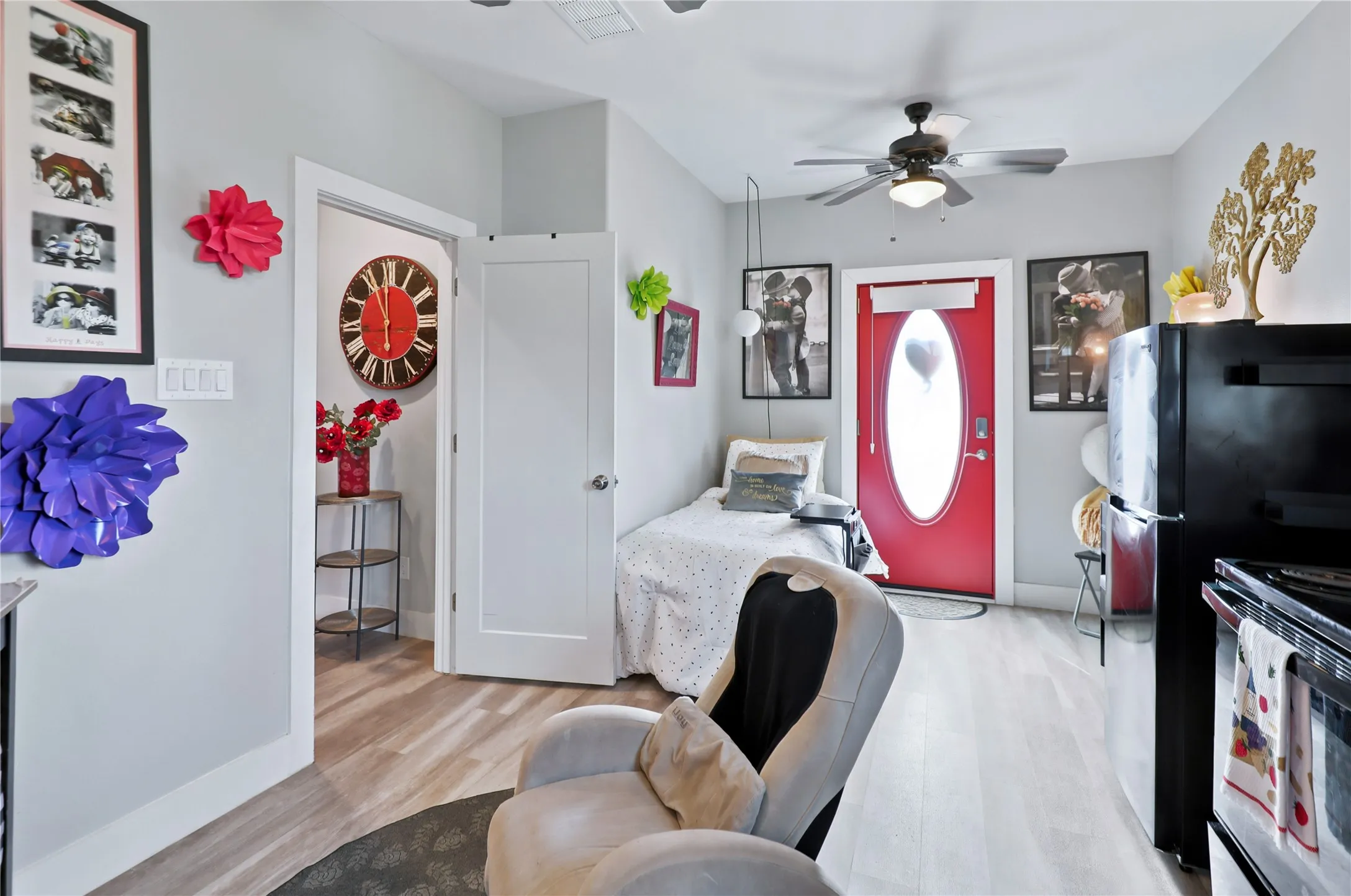 Light wood-finish flooring, a contemporary ceiling fan with integrated lighting, and a red entry door with an oval glass insert