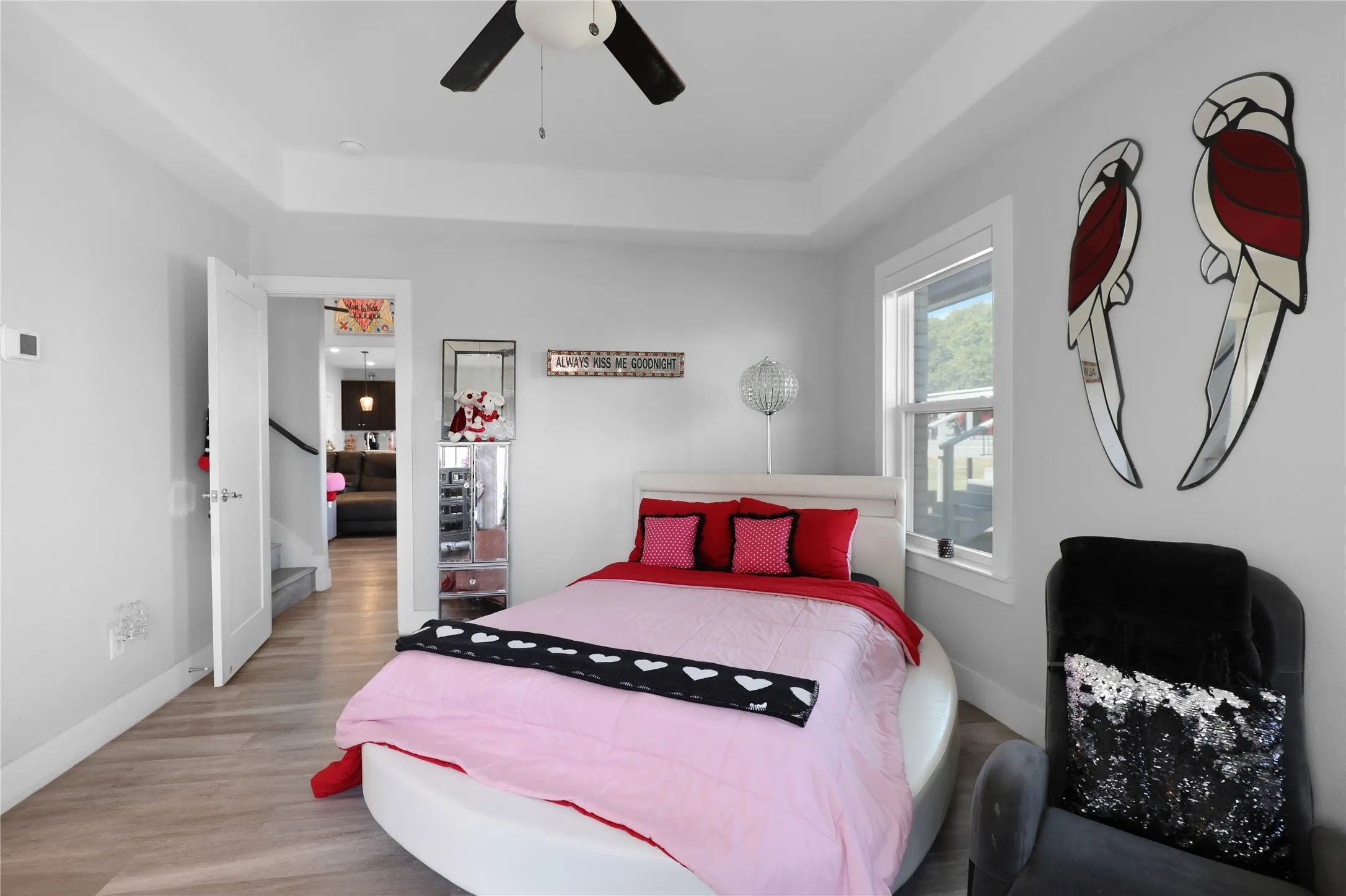 Recessed ceiling with a central ceiling fan, light wood-finish flooring, and a single window with white trim