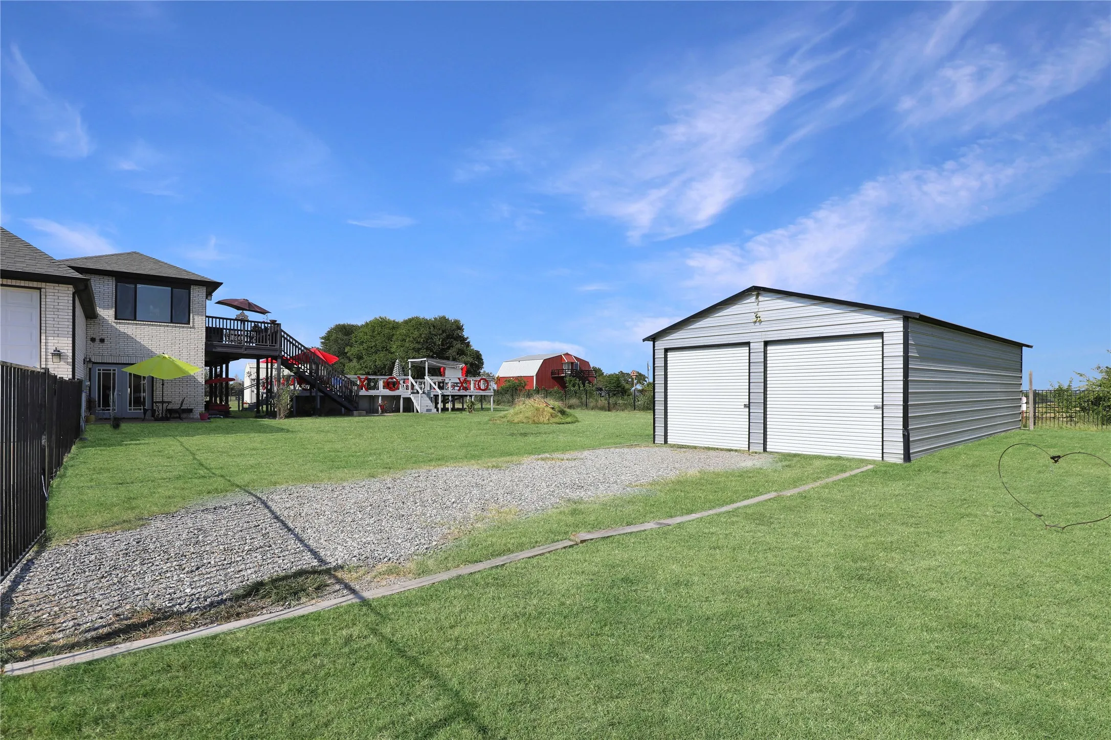 Detached two-car garage with roll-up doors, gravel parking area, and expansive lawn