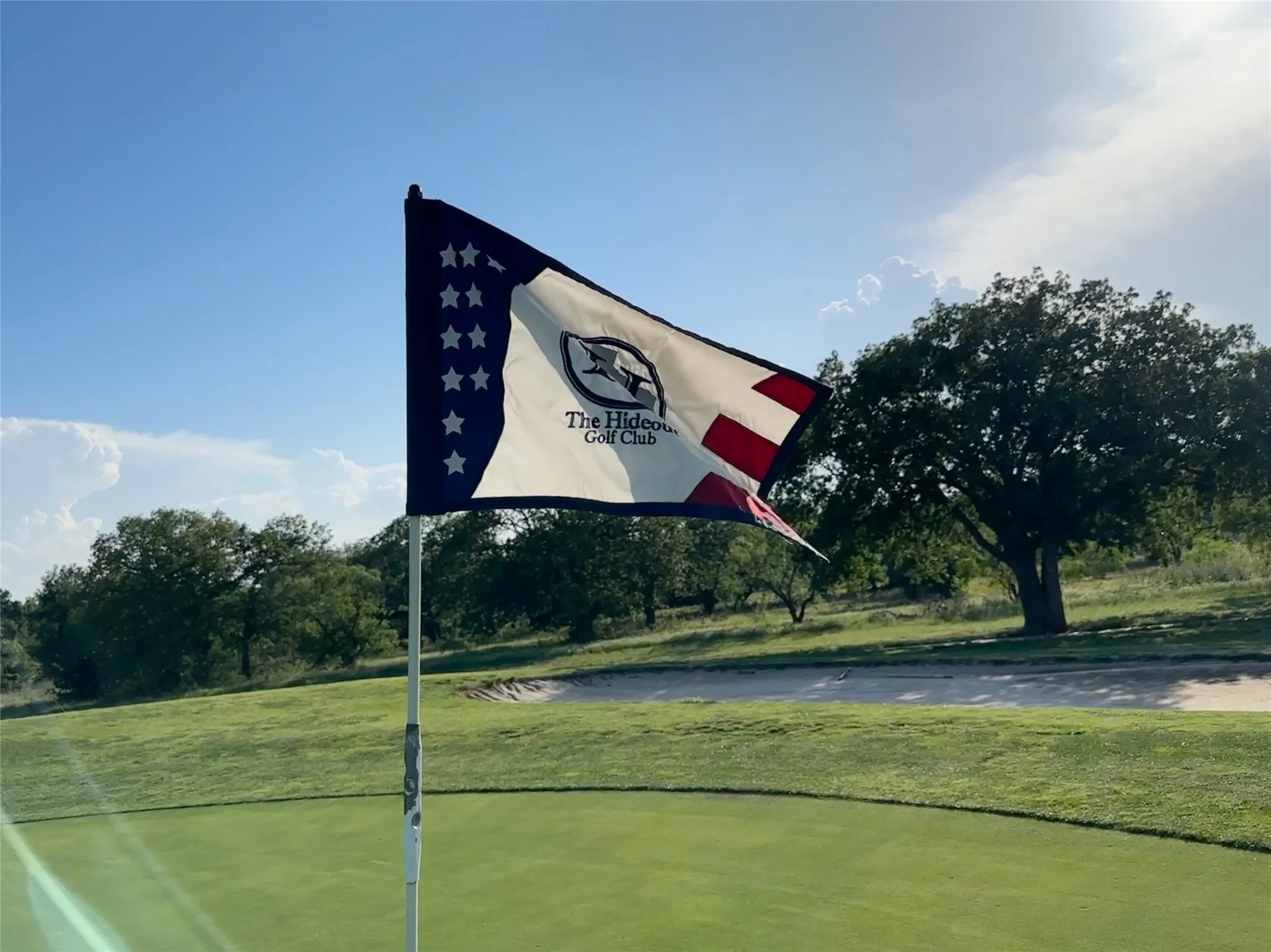 Golf course setting featuring a putting green, mature trees, and a sand trap