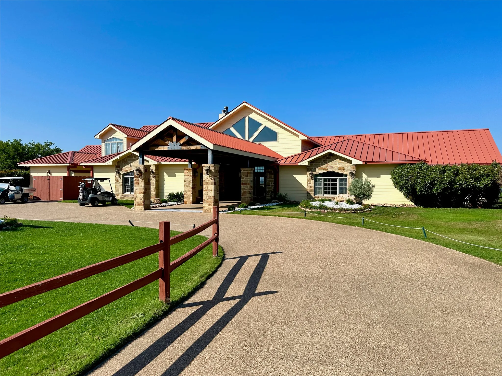 Expansive property featuring a curved aggregate driveway, a red metal roof, and stone-clad architectural elements