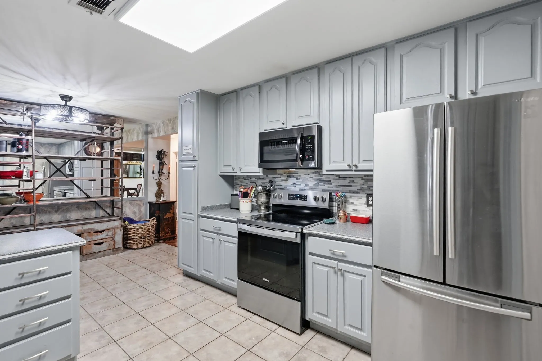 Recessed lighting, tile flooring, stainless steel appliances, light gray cabinetry, and a skylight