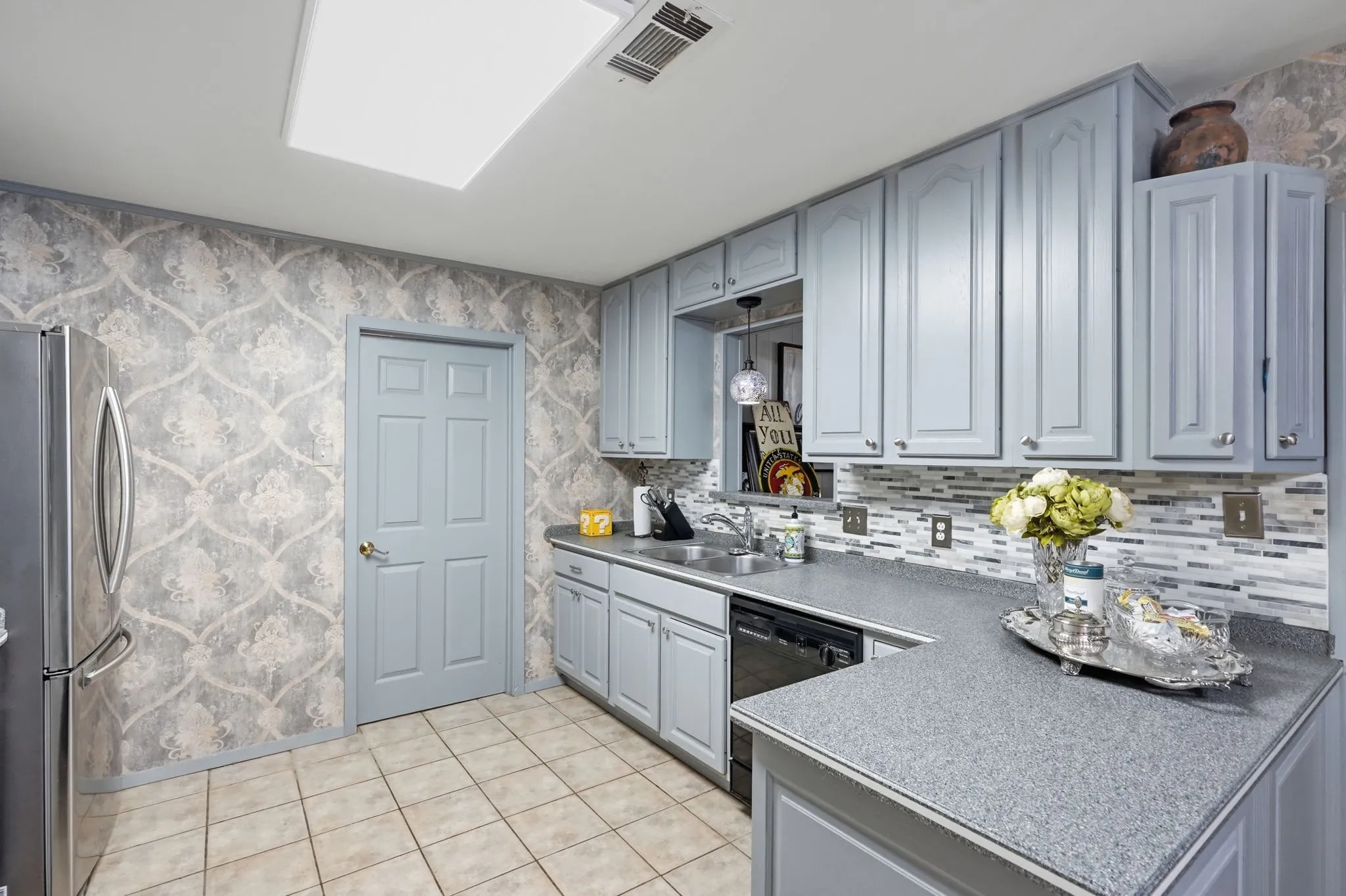 Kitchen featuring light blue cabinetry, mosaic tile backsplash, solid surface countertops, a stainless steel refrigerator, and tiled flooring